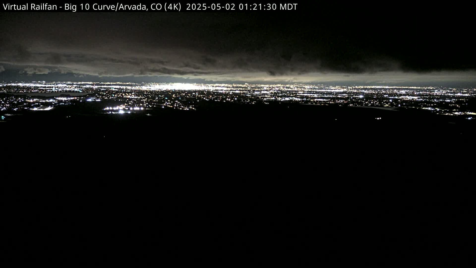 A nighttime view of a city skyline illuminated by numerous lights under a cloudy sky.