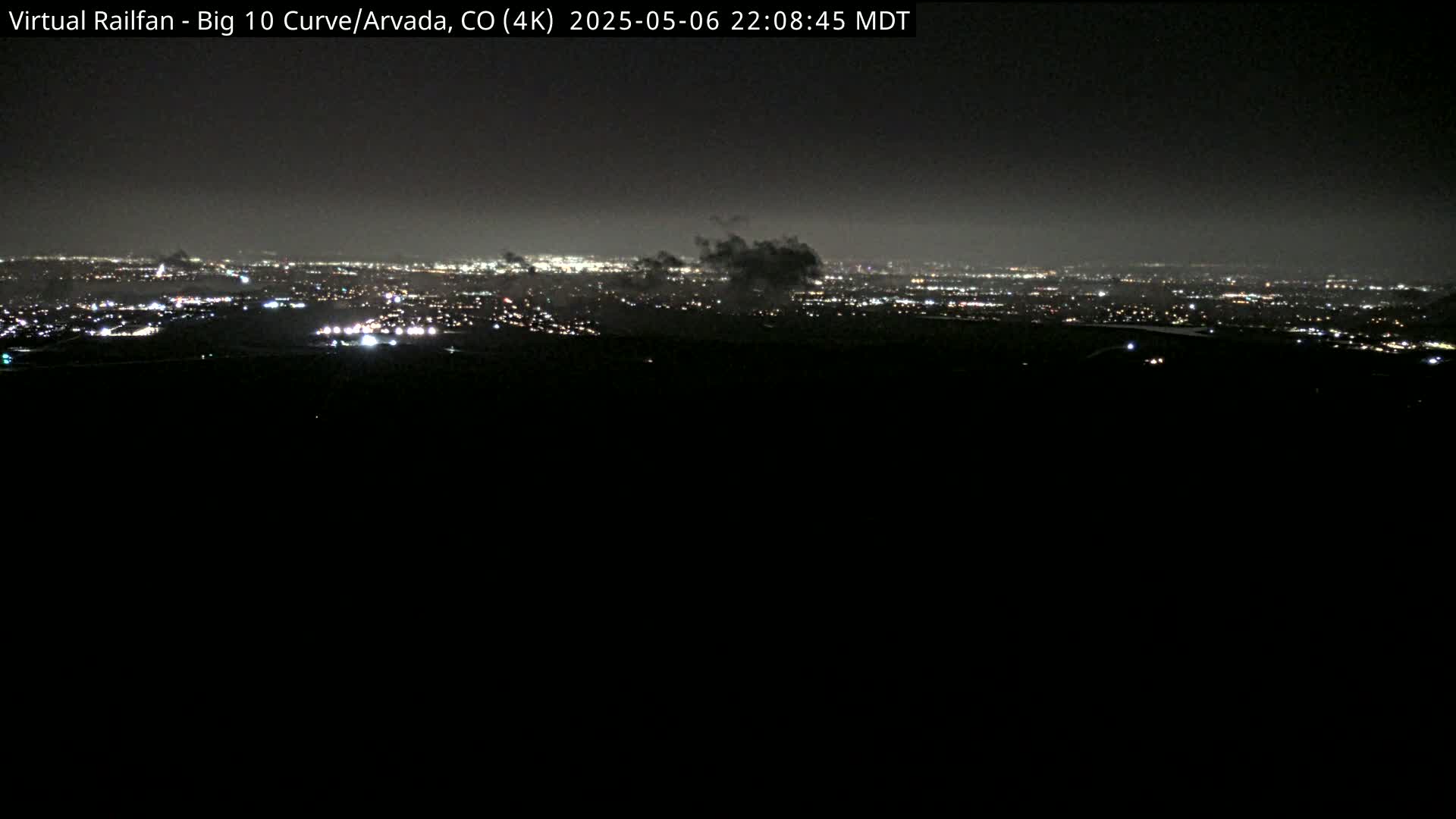 A nighttime long shot shows a distant city skyline illuminated with lights under a hazy, dark sky.