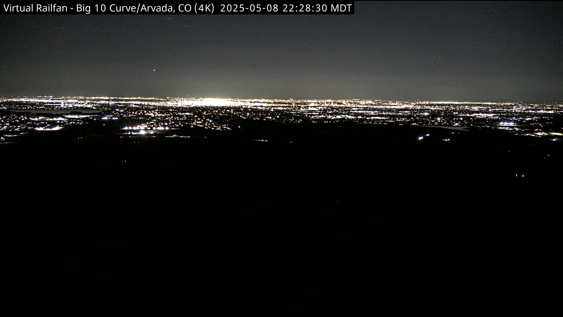 A nighttime long shot shows a distant city illuminated by countless lights under a clear, dark sky.