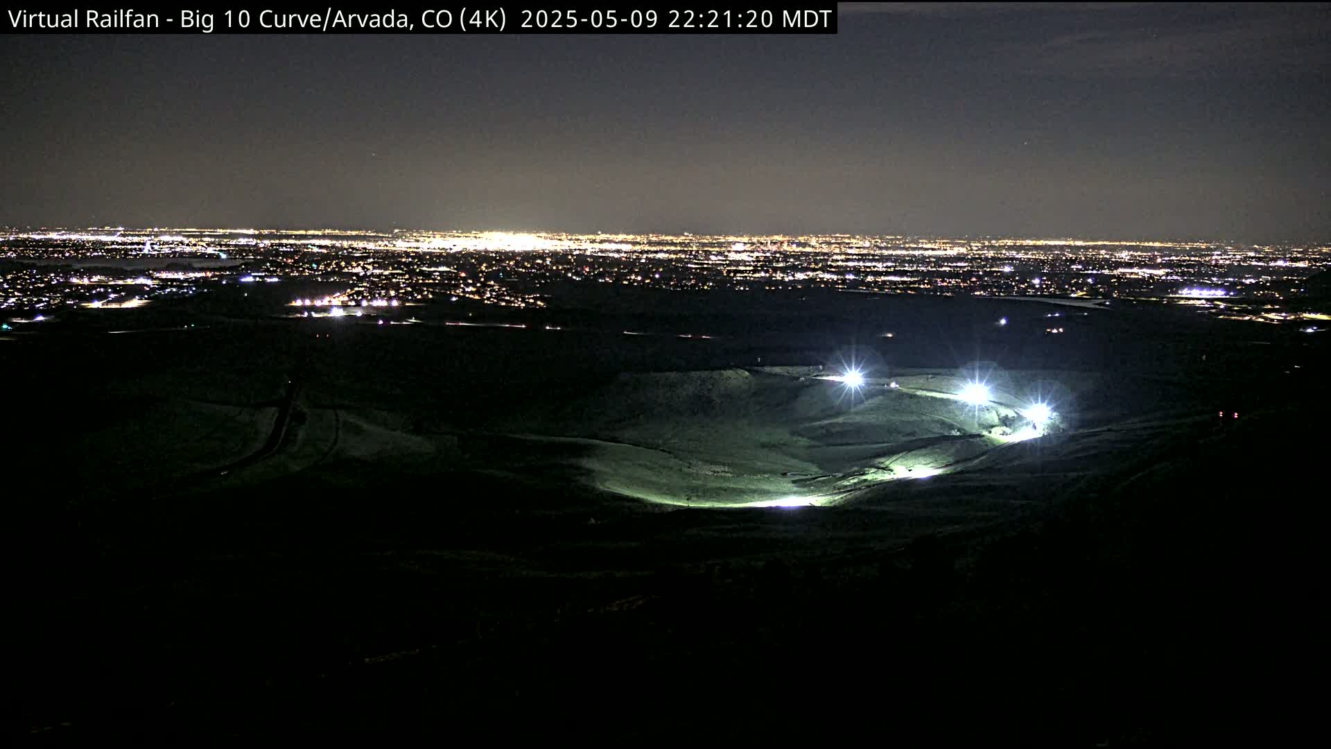 A nighttime view of a brightly lit area on a hill overlooking a distant city.