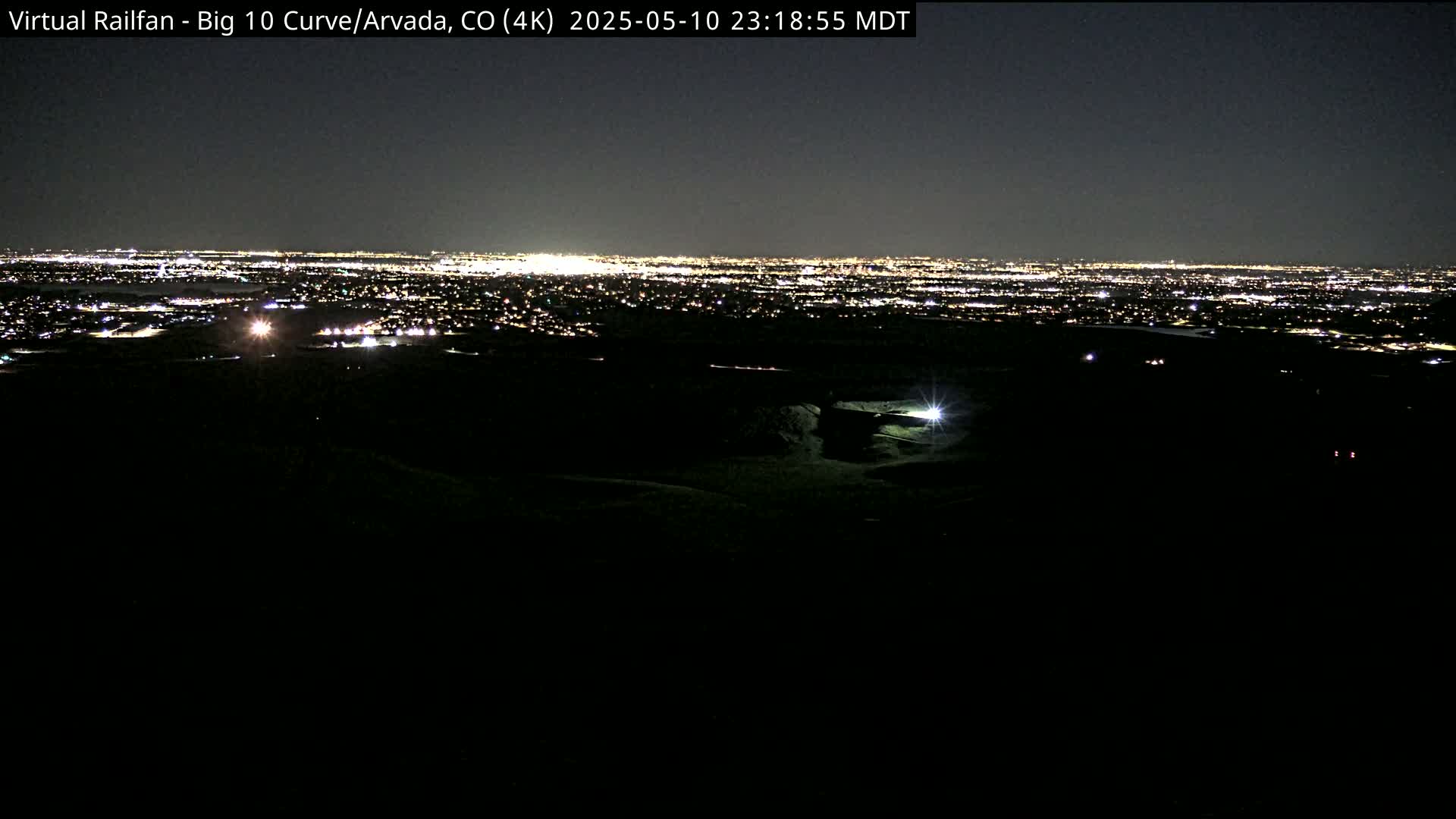 A nighttime view shows a distant city illuminated by lights, observed from a dark, elevated vantage point.