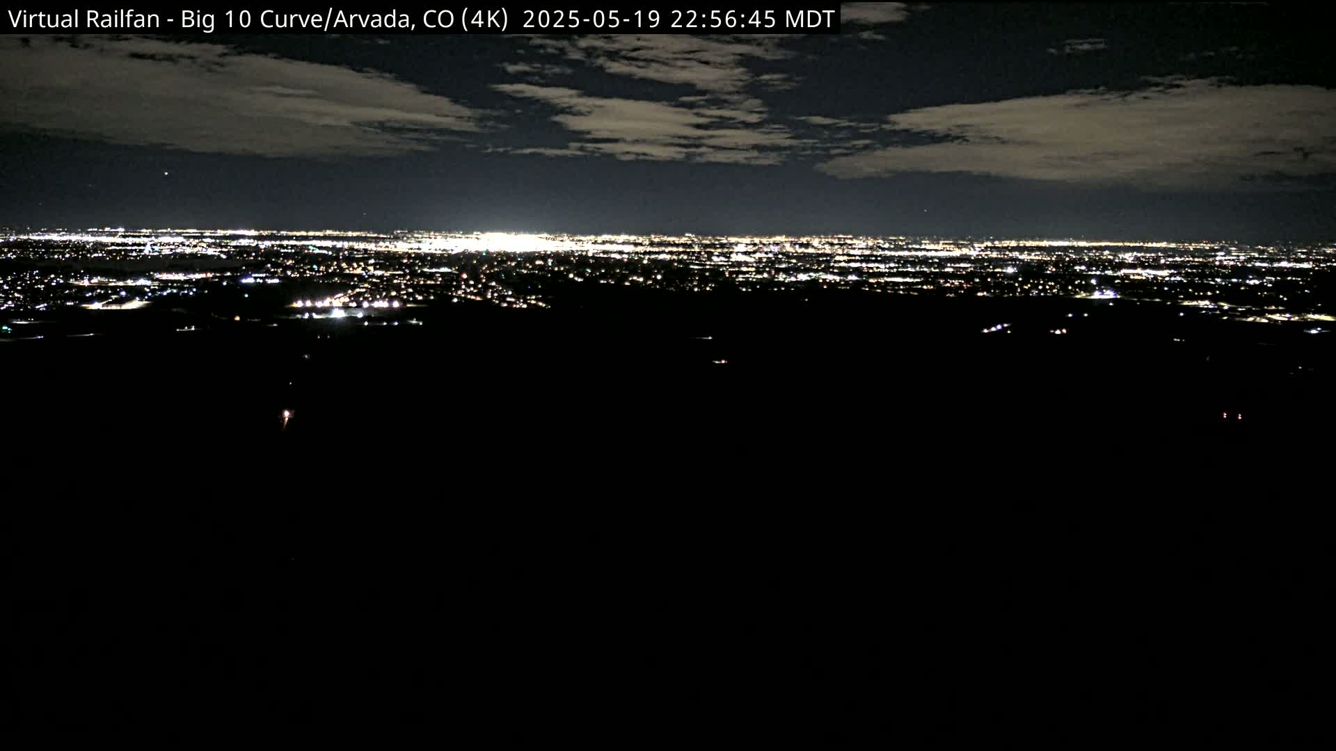 A nighttime view of a sprawling city illuminated by countless lights under a partly cloudy sky.