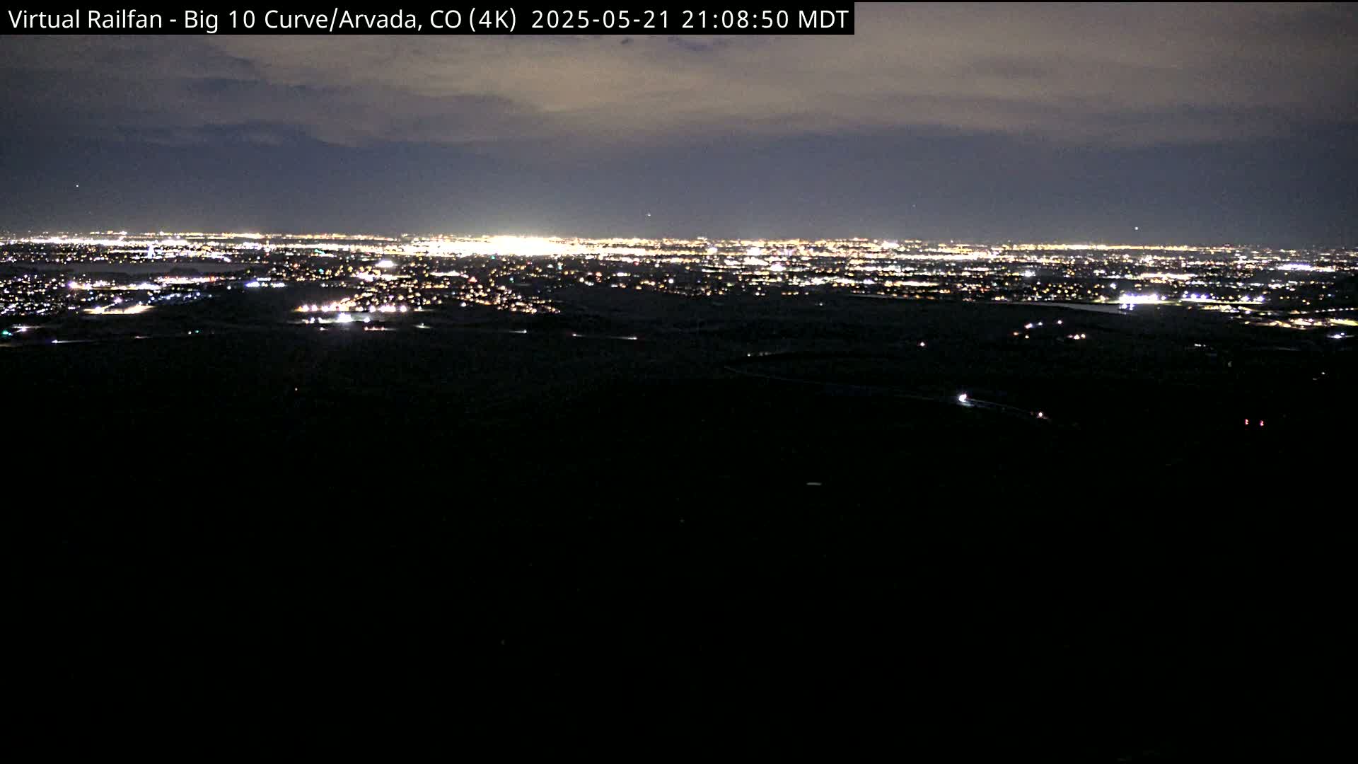 A nighttime view of a sprawling city illuminated by countless lights under a partly cloudy sky.