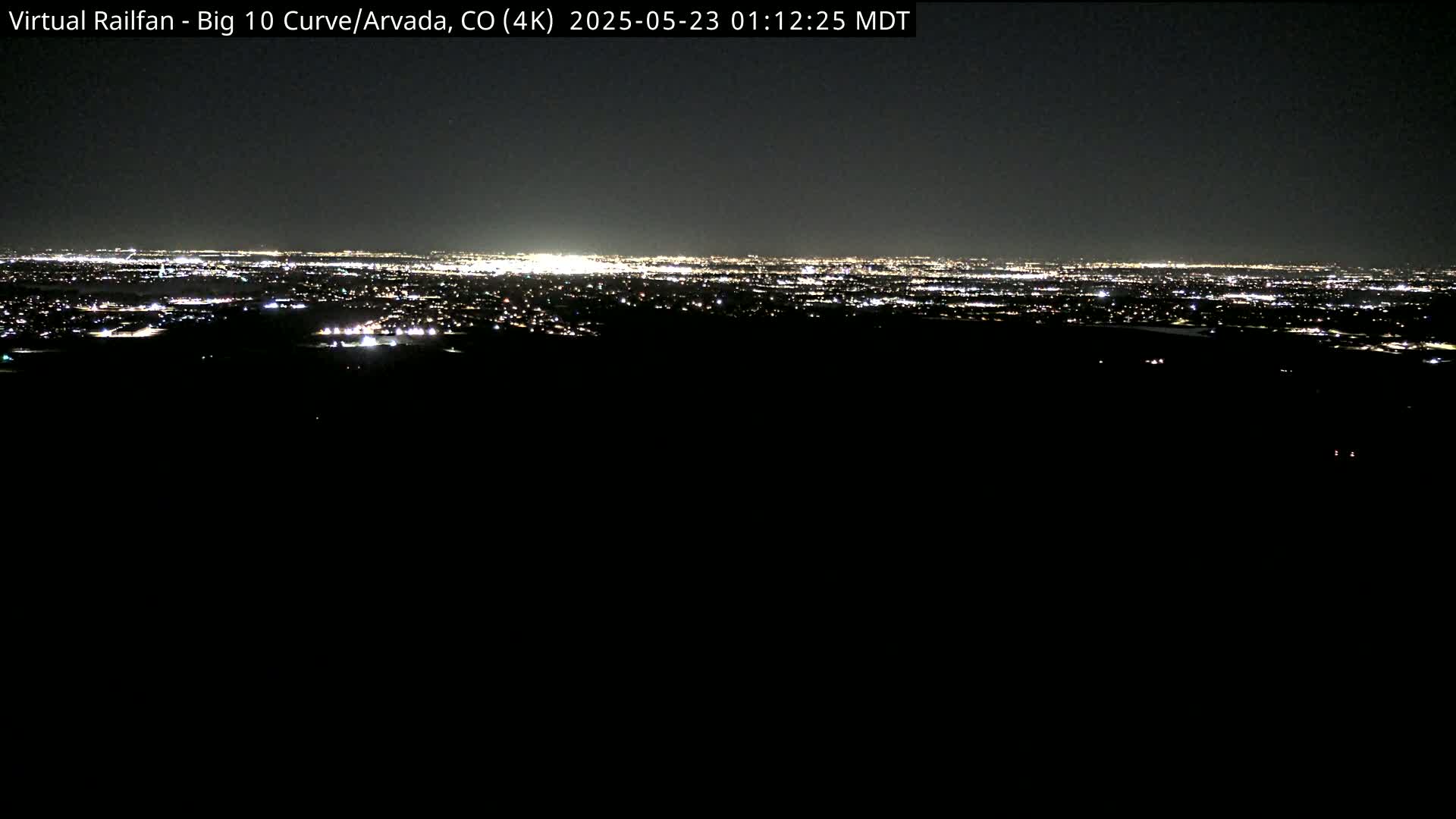 A nighttime long shot shows a distant city skyline illuminated by countless lights under a dark sky.