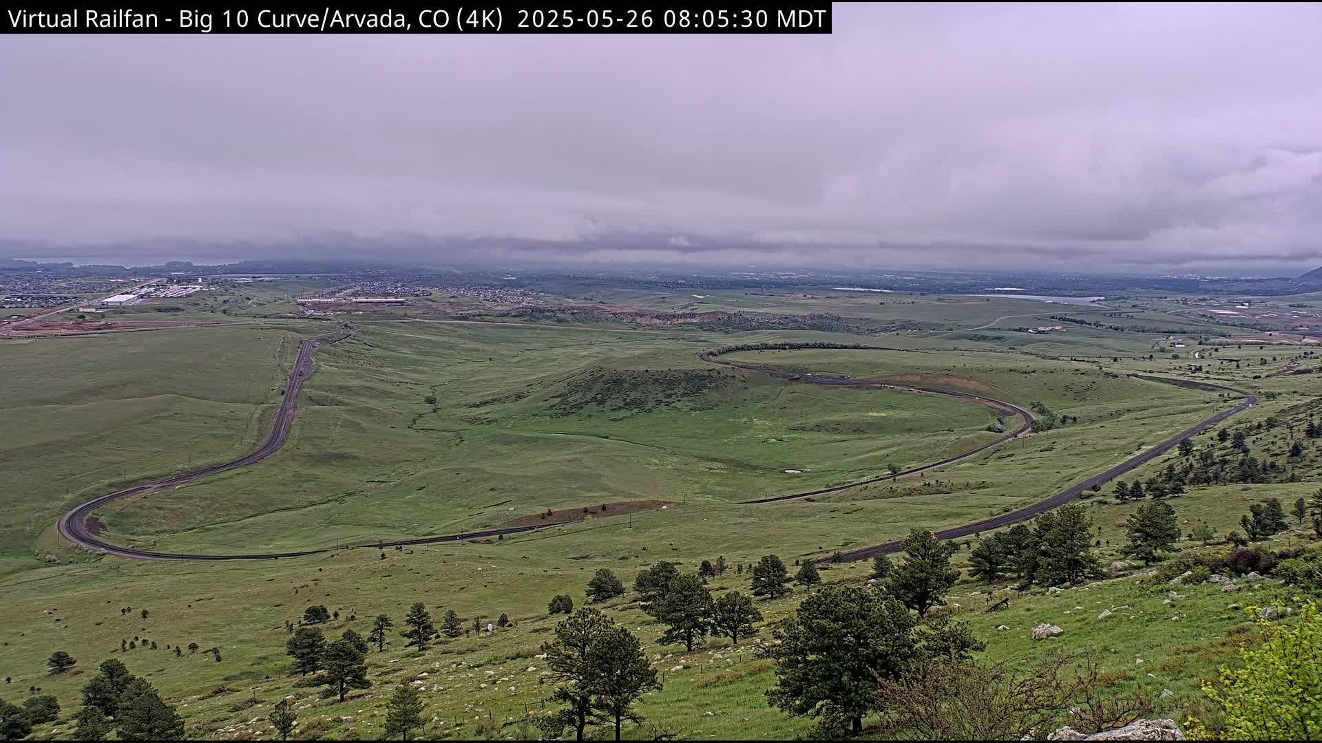 A winding road curves through a vast, green landscape under an overcast sky.