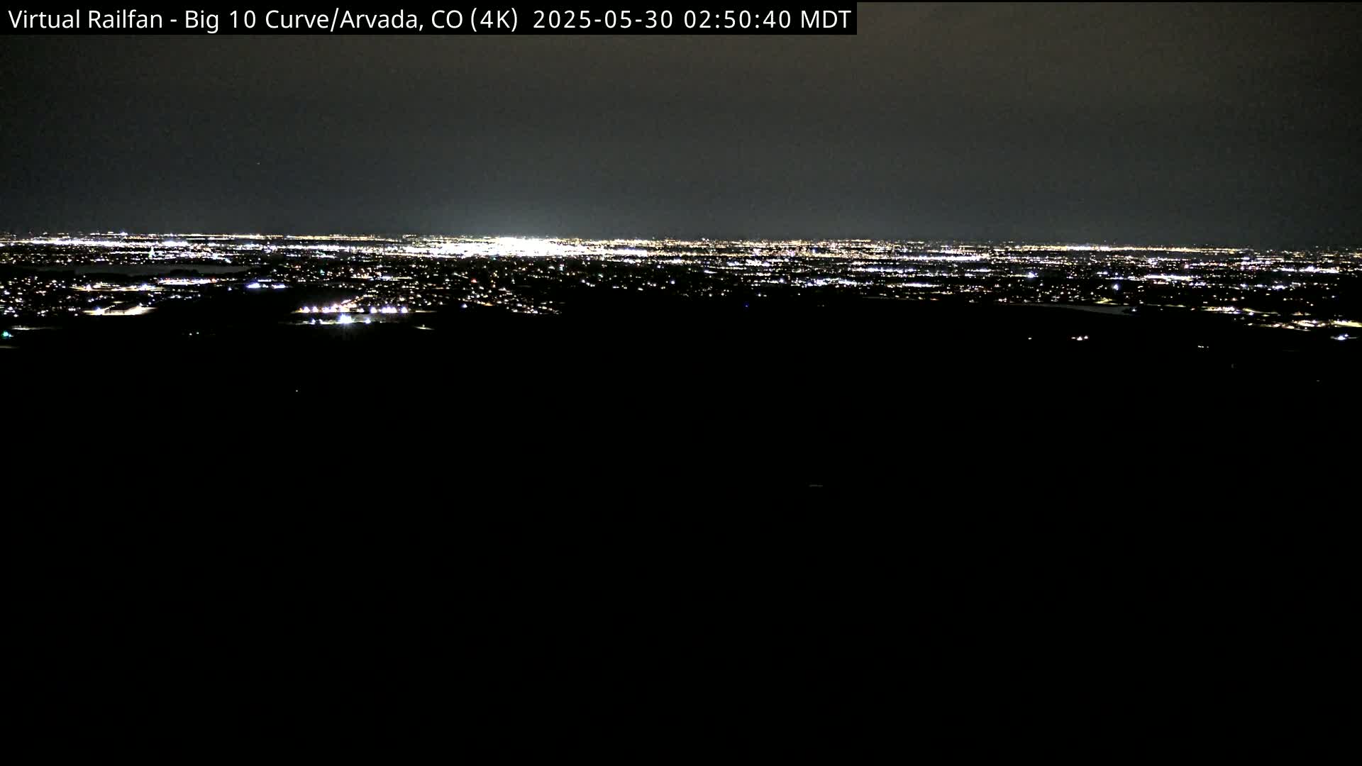 A nighttime view of a sprawling city illuminated by countless lights, seen from a dark vantage point.