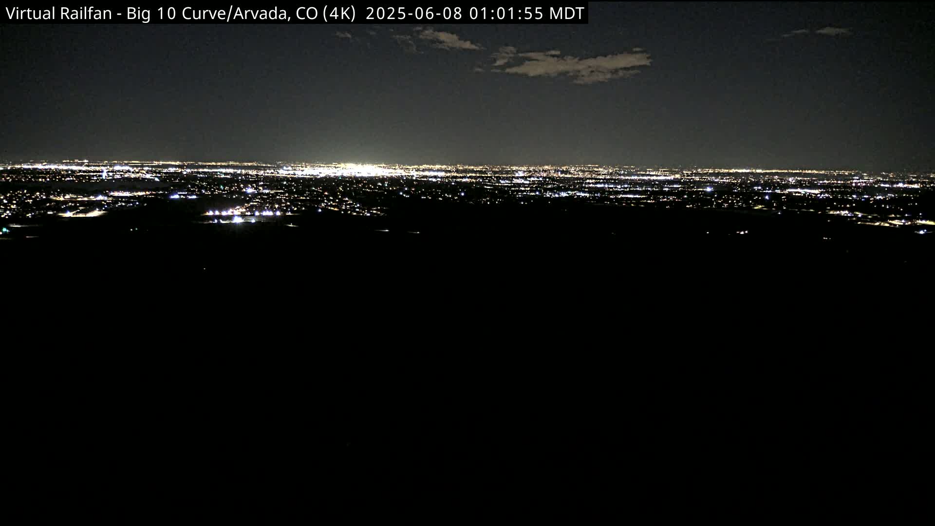 A nighttime, long-range view of a sprawling city illuminated by countless lights under a mostly clear sky.