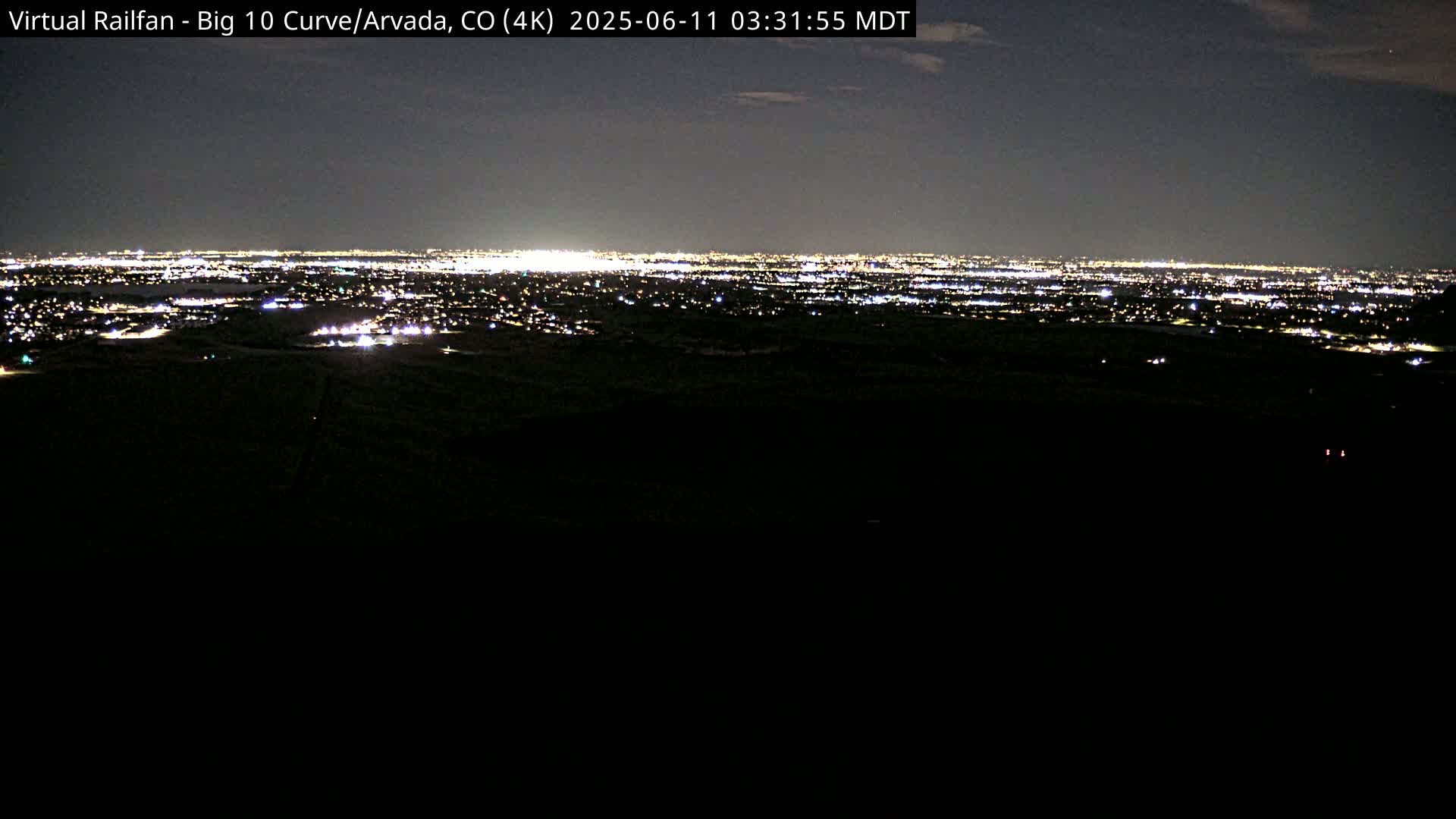 A nighttime, long-range view of a city's lights spread across a dark landscape under a mostly clear sky.