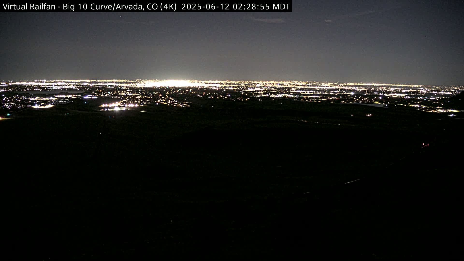 A nighttime long shot shows a sprawling city illuminated by countless lights in the distance, under a clear, dark sky.