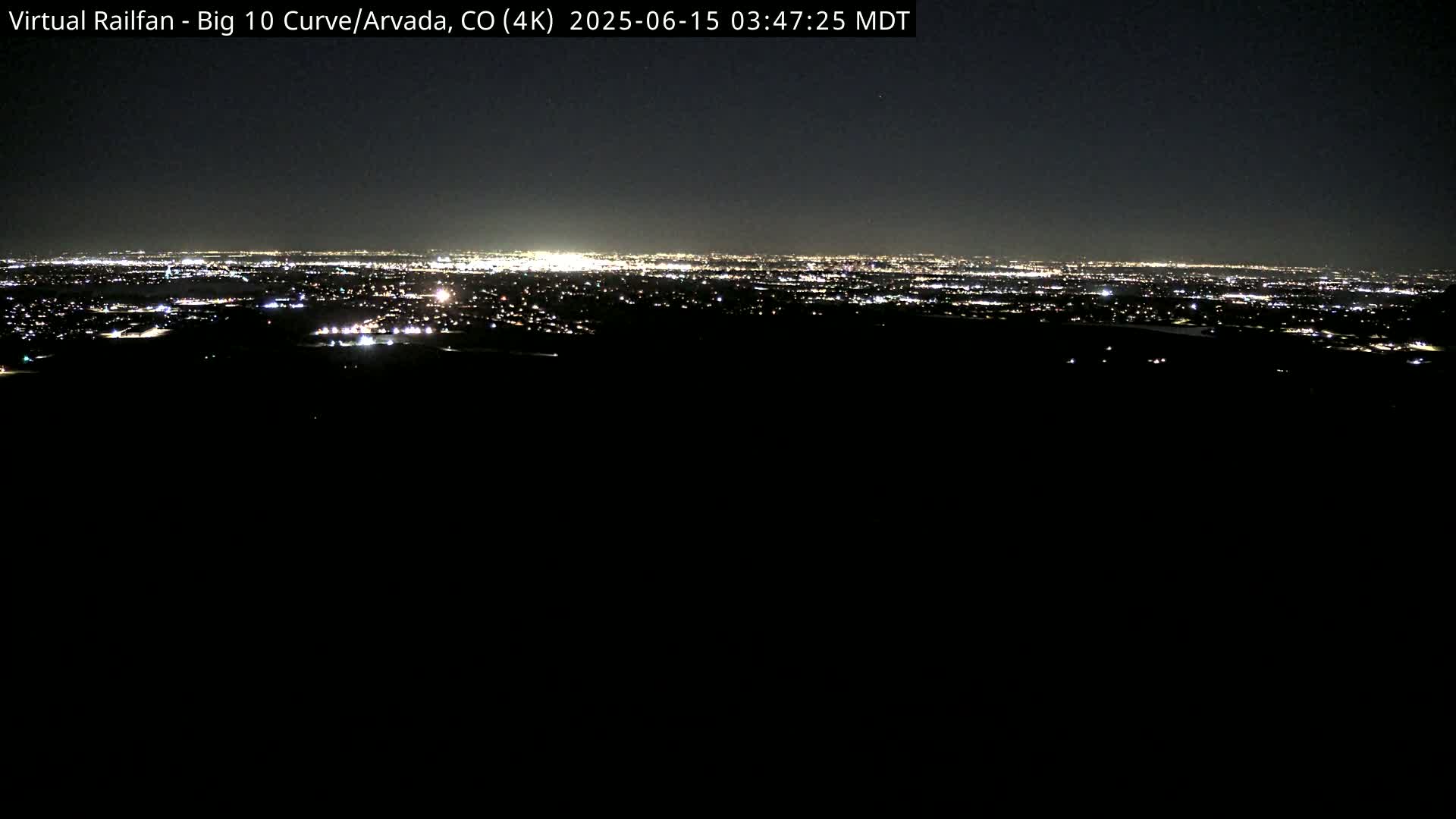 A nighttime long shot shows a sprawling city's lights on the horizon from a dark, elevated vantage point.