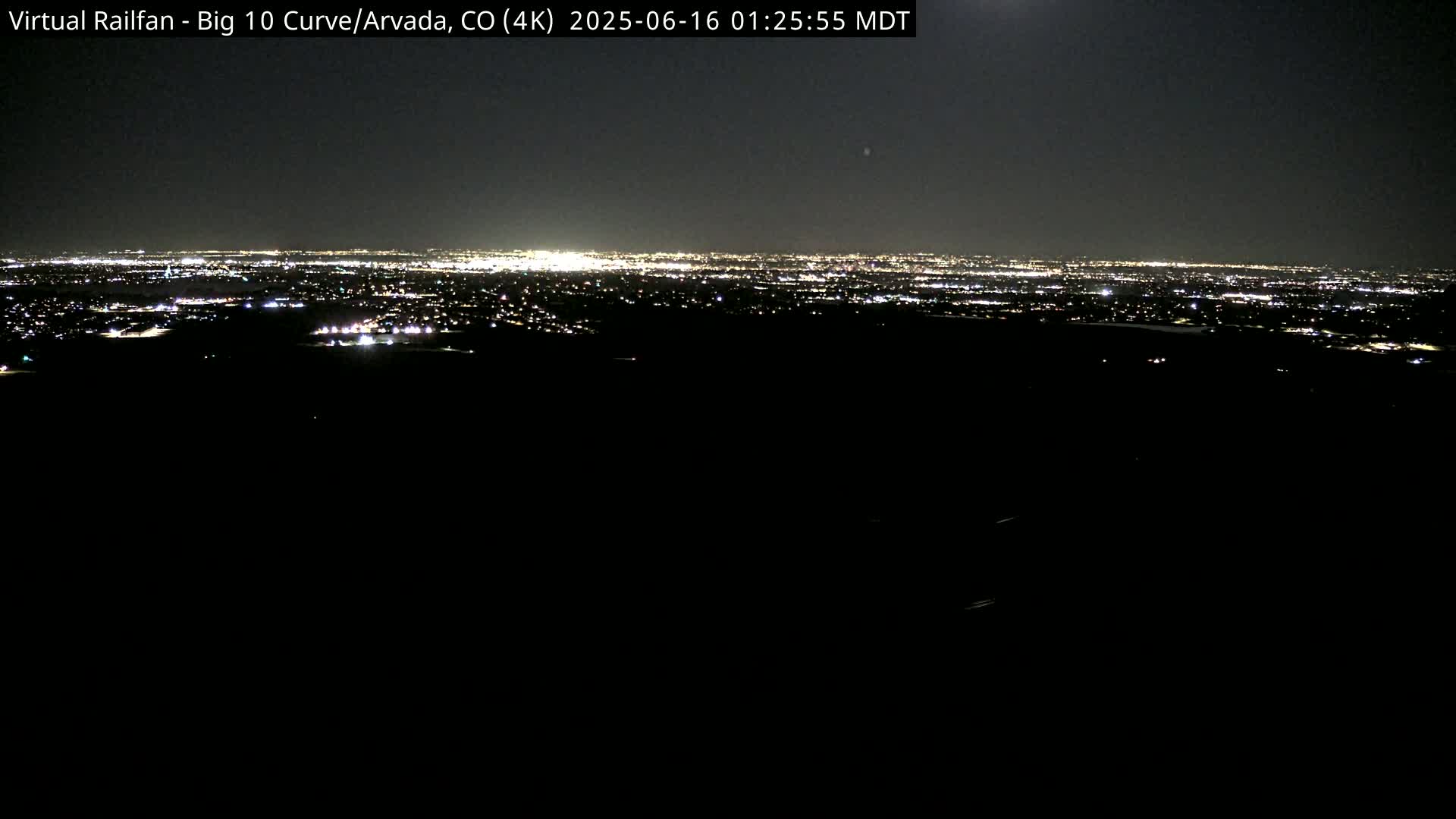 A nighttime, long-range view of a city's lights spread across a dark landscape under a clear, moonlit sky.