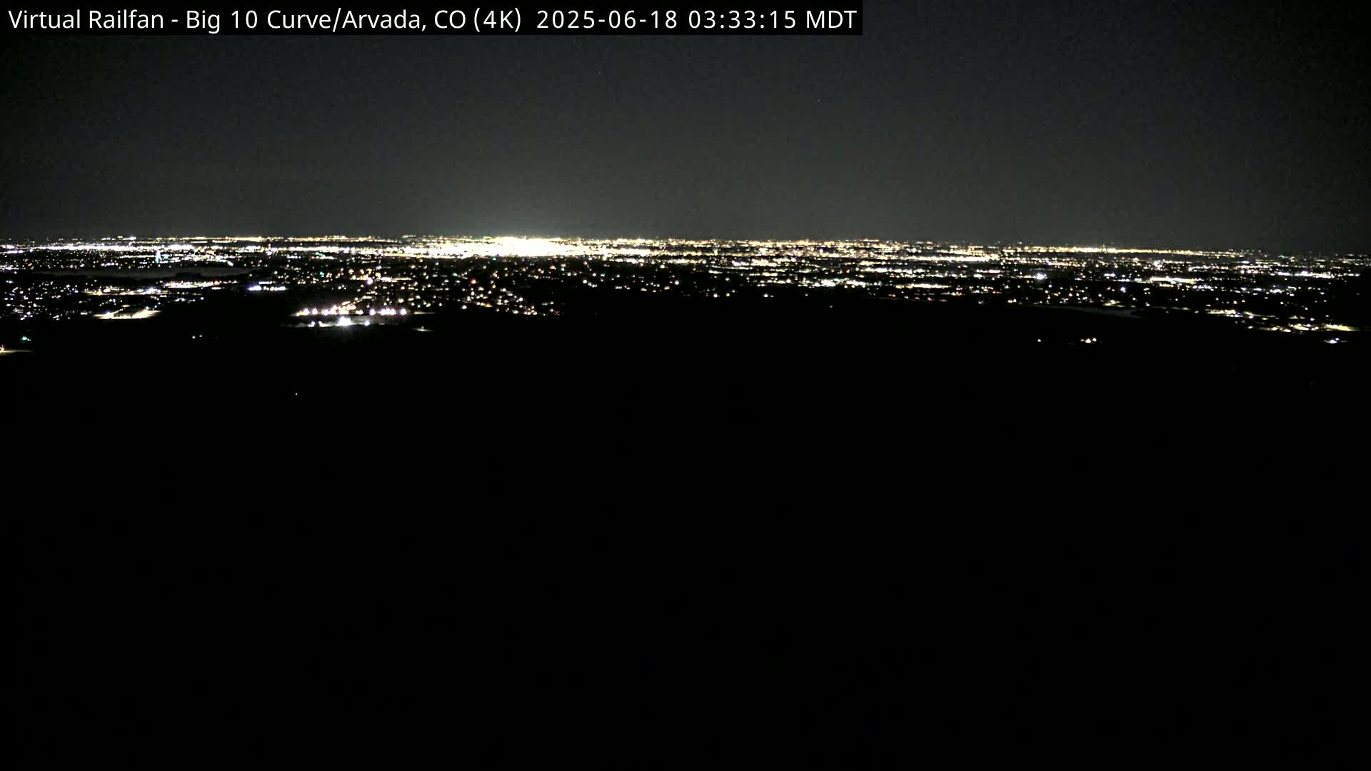 A nighttime long shot shows a distant city skyline illuminated by numerous lights under a dark sky.