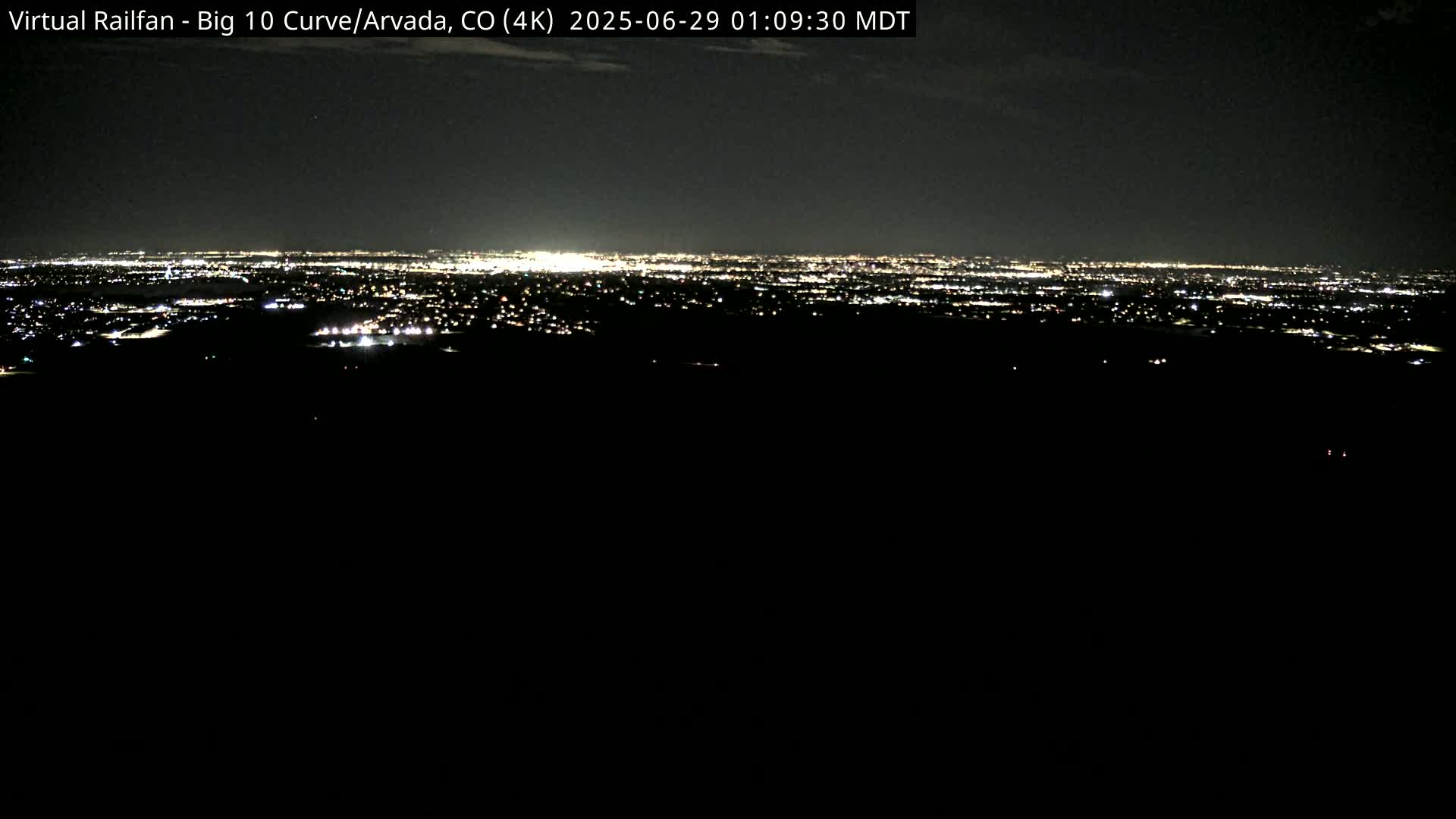 A distant city's lights illuminate the night sky from a dark, elevated vantage point.
