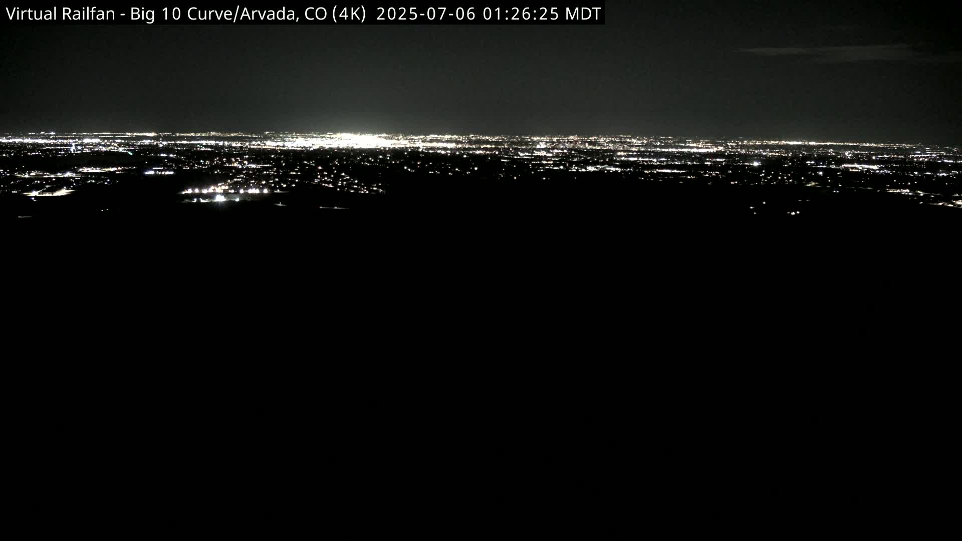 A nighttime long shot shows a distant city skyline illuminated by numerous lights under a dark sky.