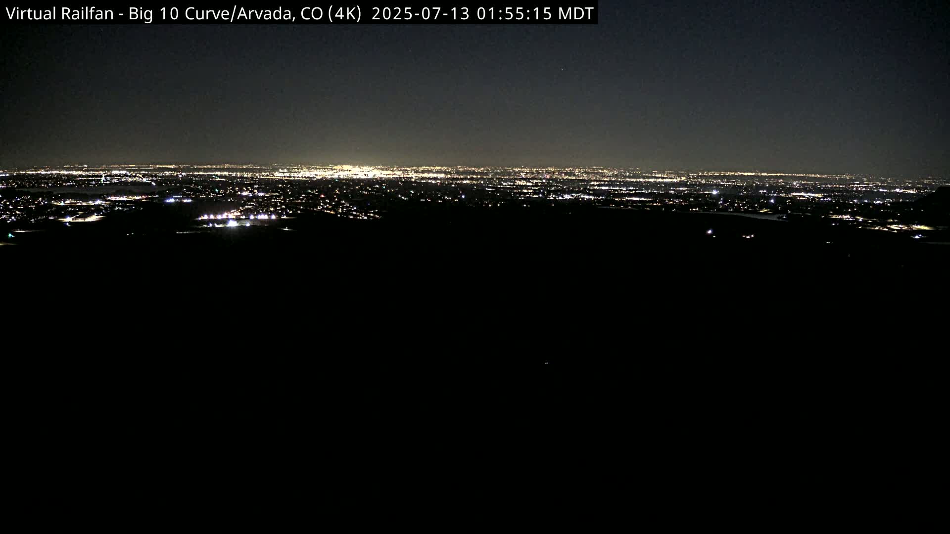 A nighttime long shot shows a distant city skyline illuminated by lights under a clear, dark sky.
