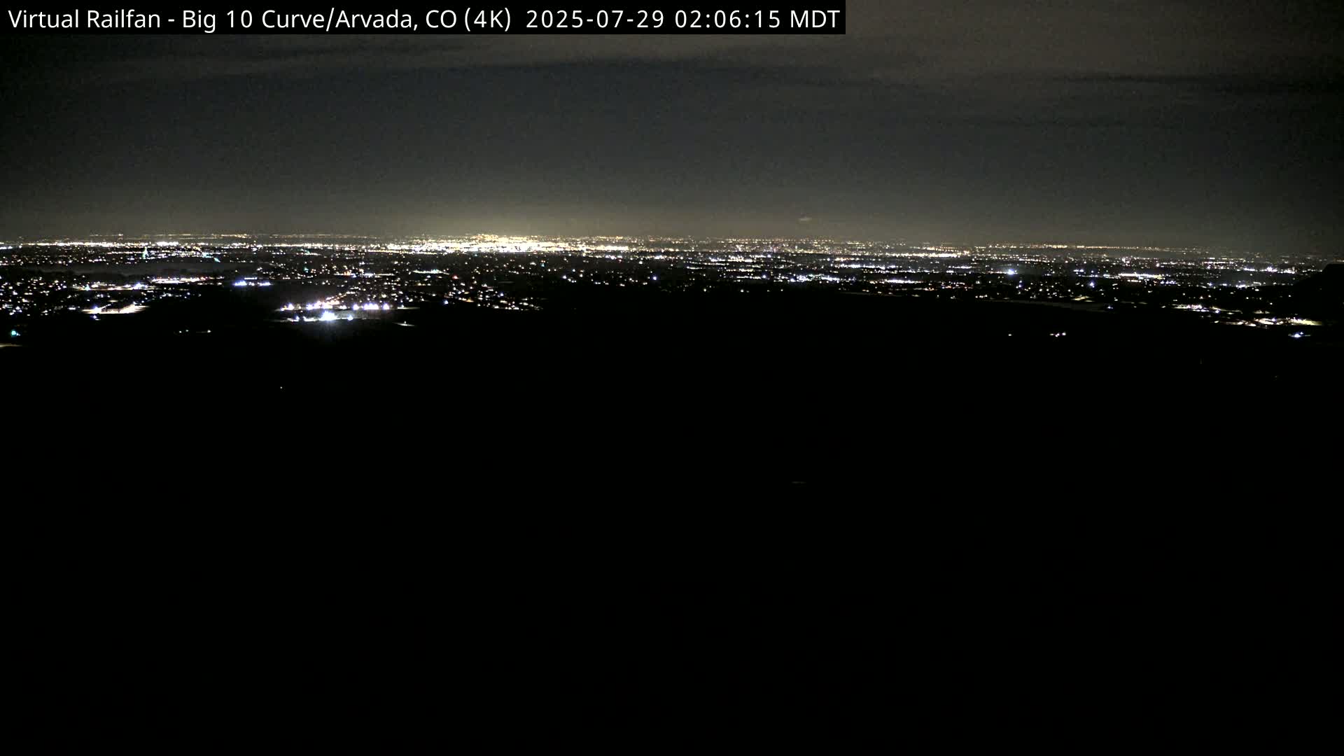 A nighttime long shot reveals a distant city skyline illuminated by lights under a dark sky.