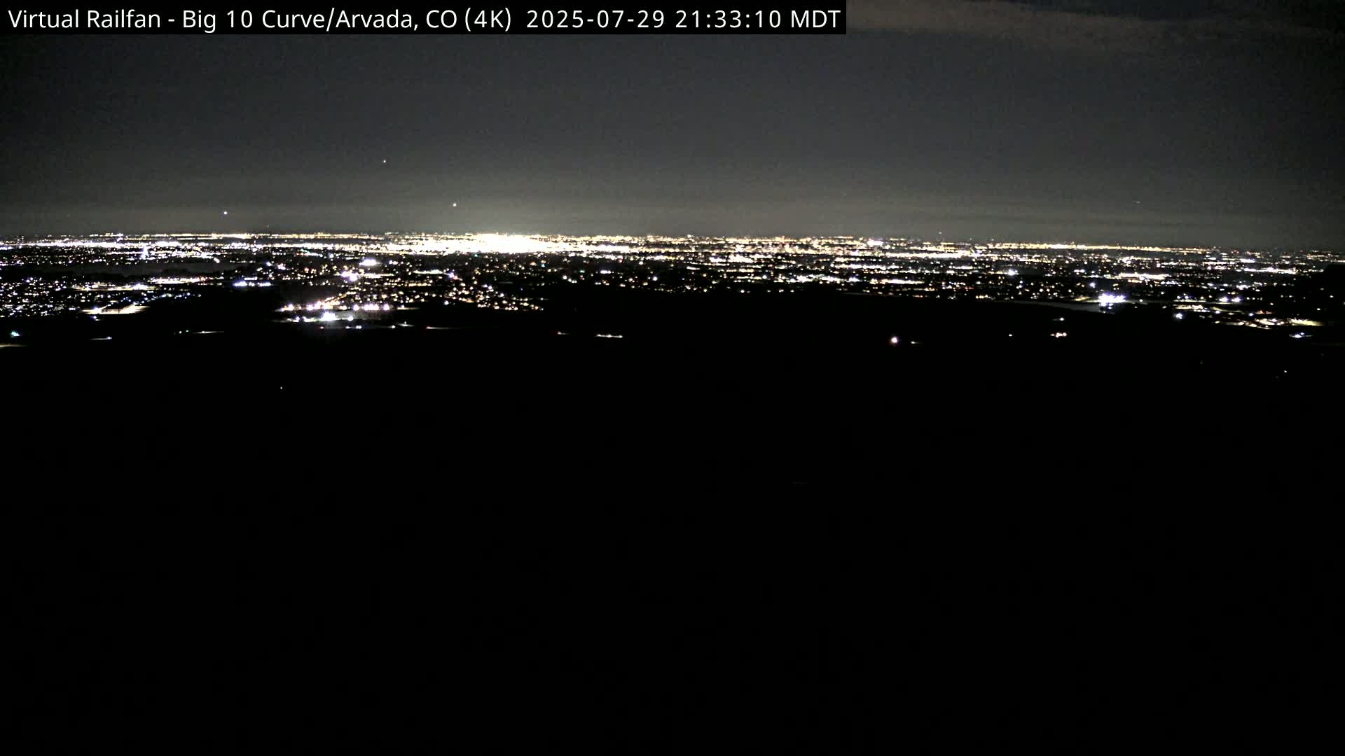 A nighttime long shot reveals a distant city skyline illuminated by lights under a dark sky.