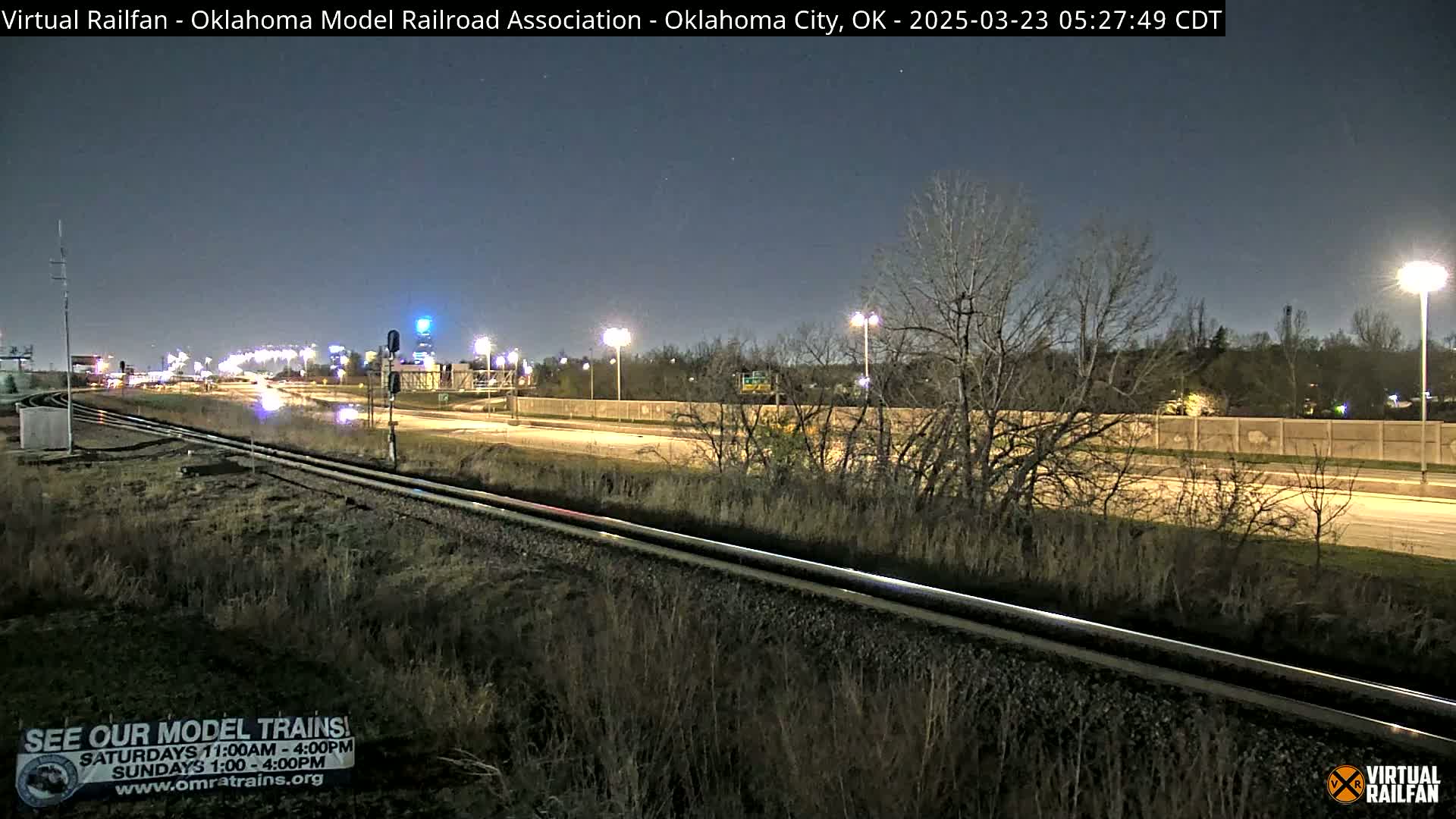 A nighttime view of railroad tracks next to a highway, under a mostly clear sky.