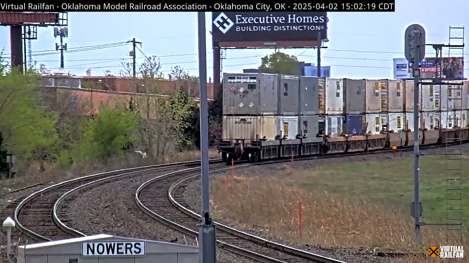 A long freight train carrying numerous shipping containers curves around a track on an overcast day.