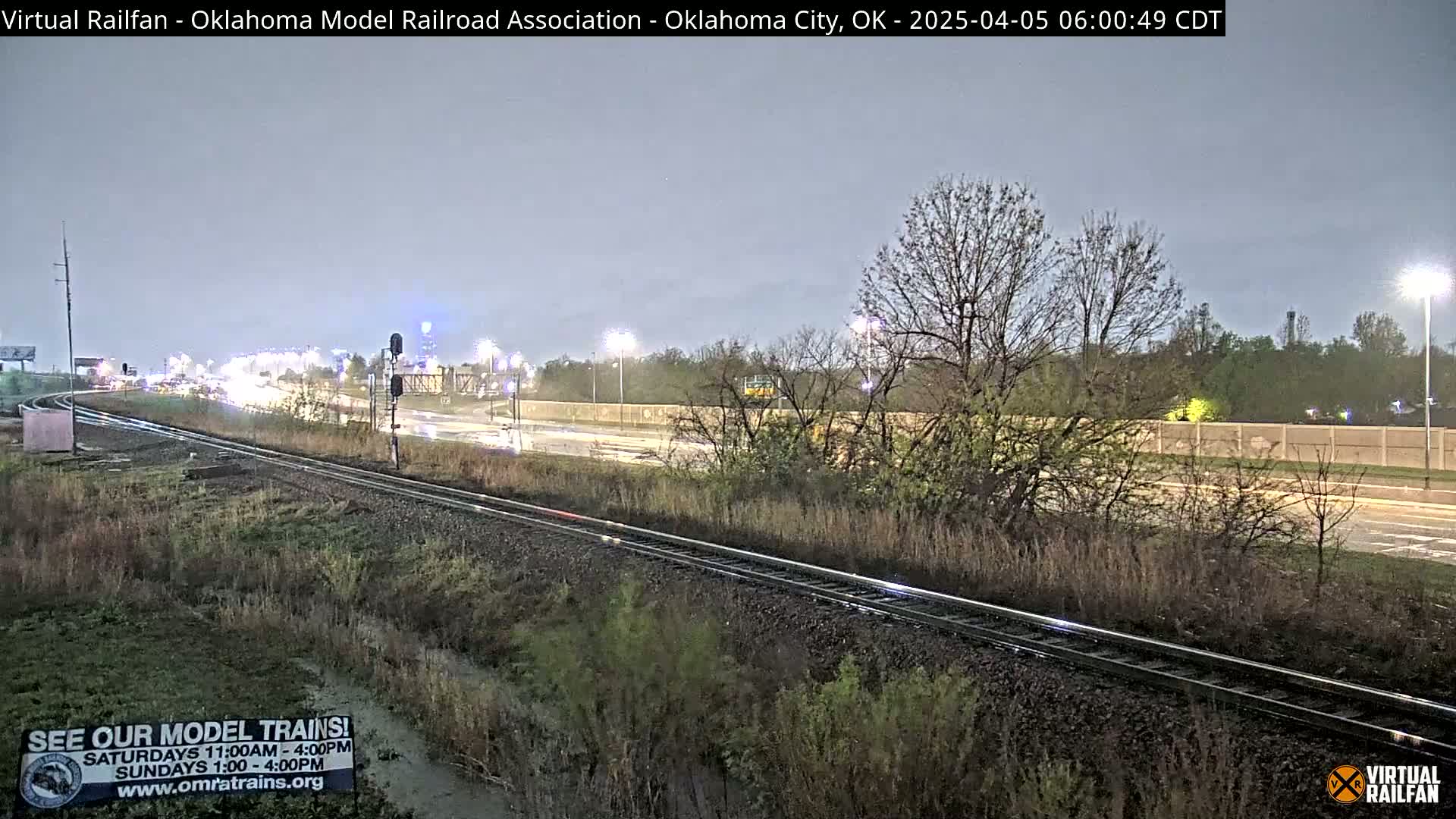 Railroad tracks run alongside a highway with light traffic under a dark, overcast sky.