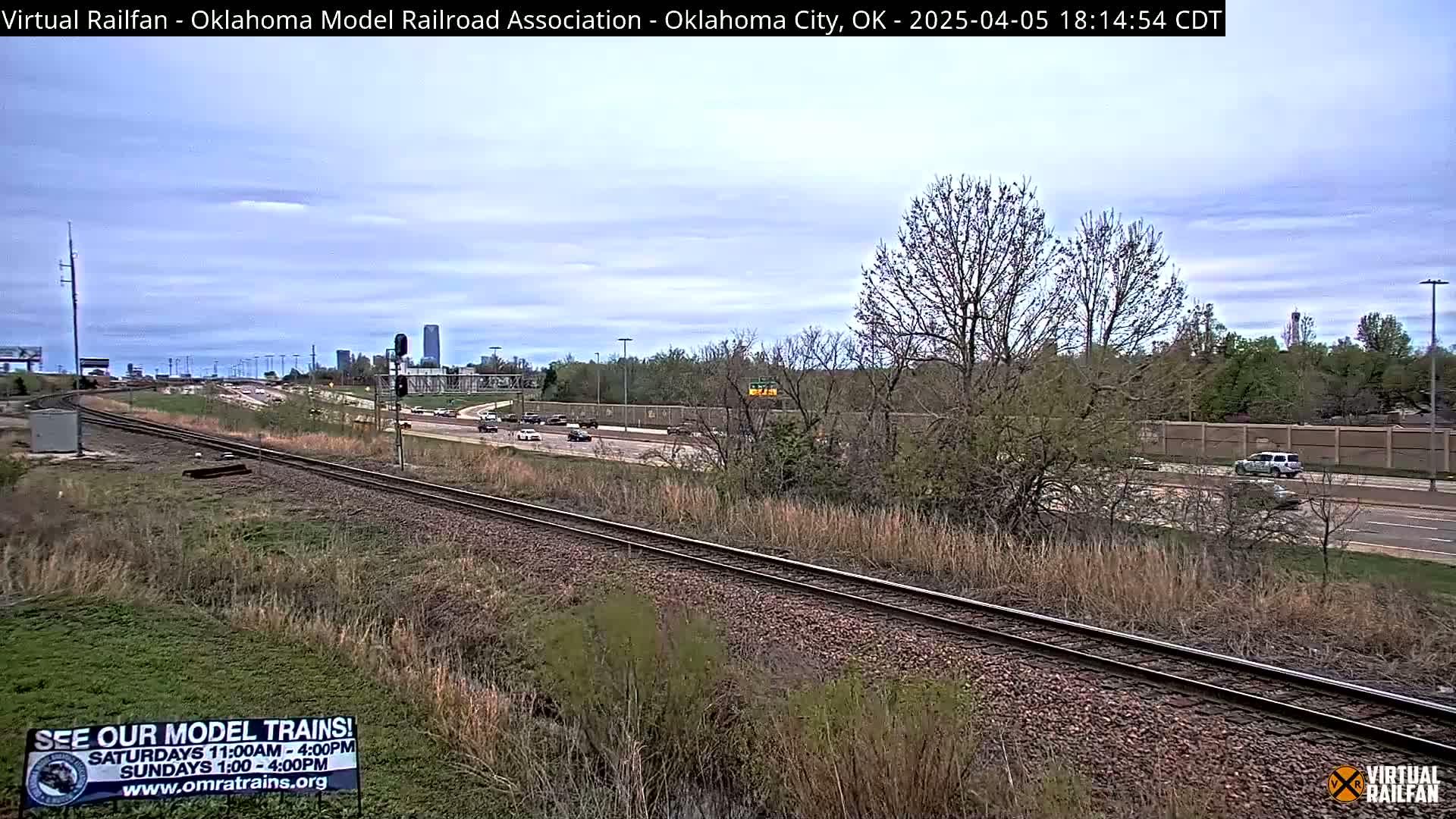 Railroad tracks run alongside a highway with sparse traffic under a partly cloudy sky.