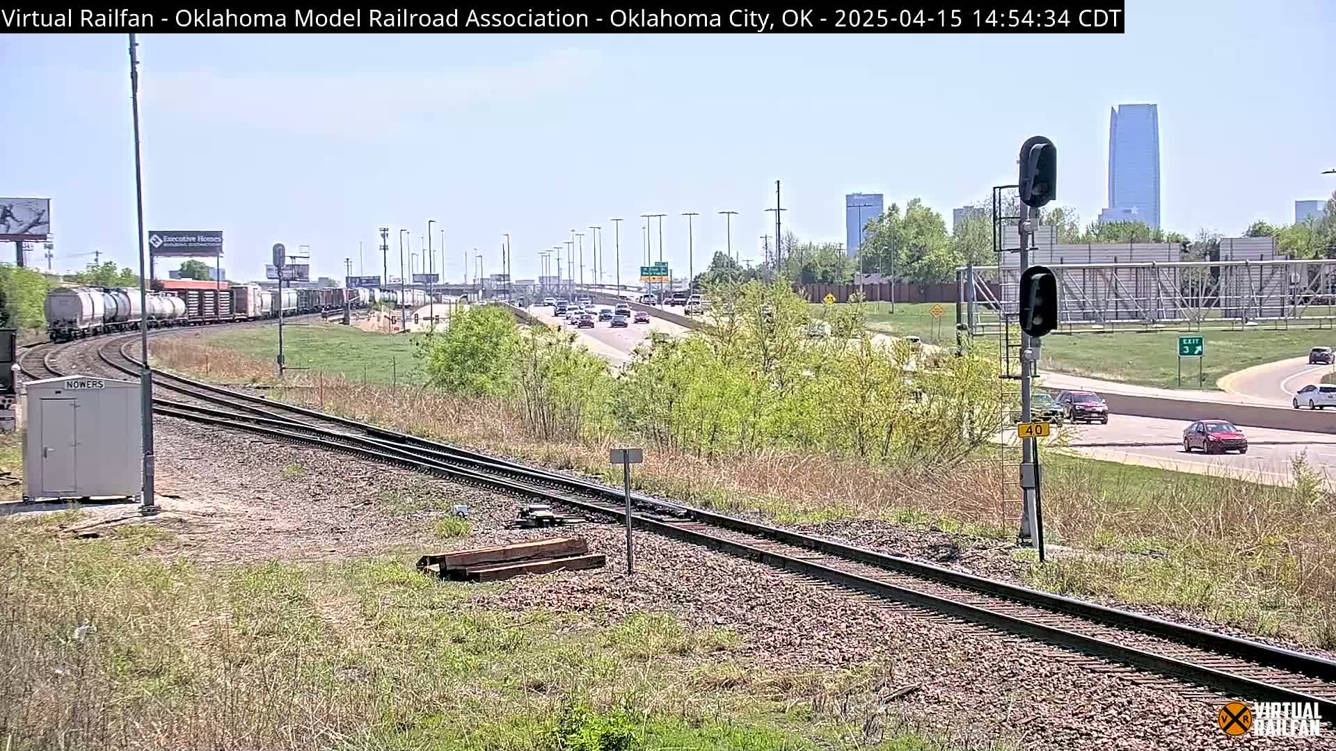 A long freight train curves past a highway with light traffic under a clear sky.