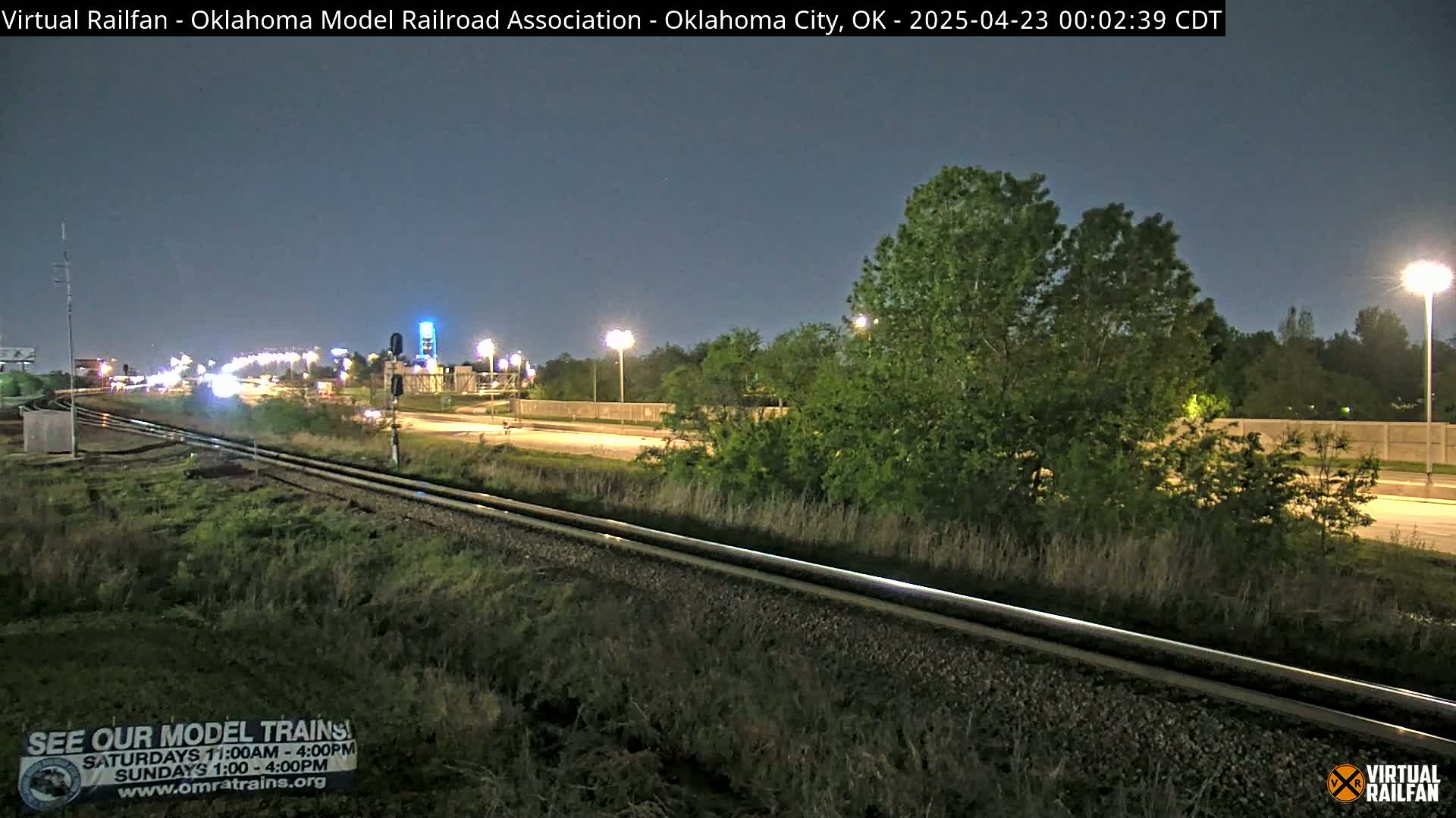 Nighttime view of railroad tracks beside a highway with some traffic under a dark, clear sky.