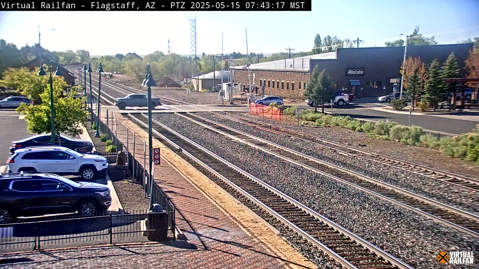 A sunny day view of multiple train tracks, a parking lot with several cars, and a building in the background.