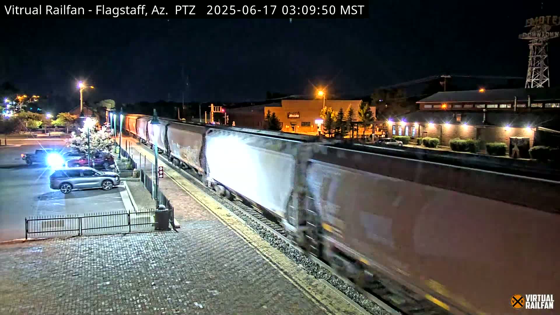 A long freight train passes through a station at night under a clear sky.
