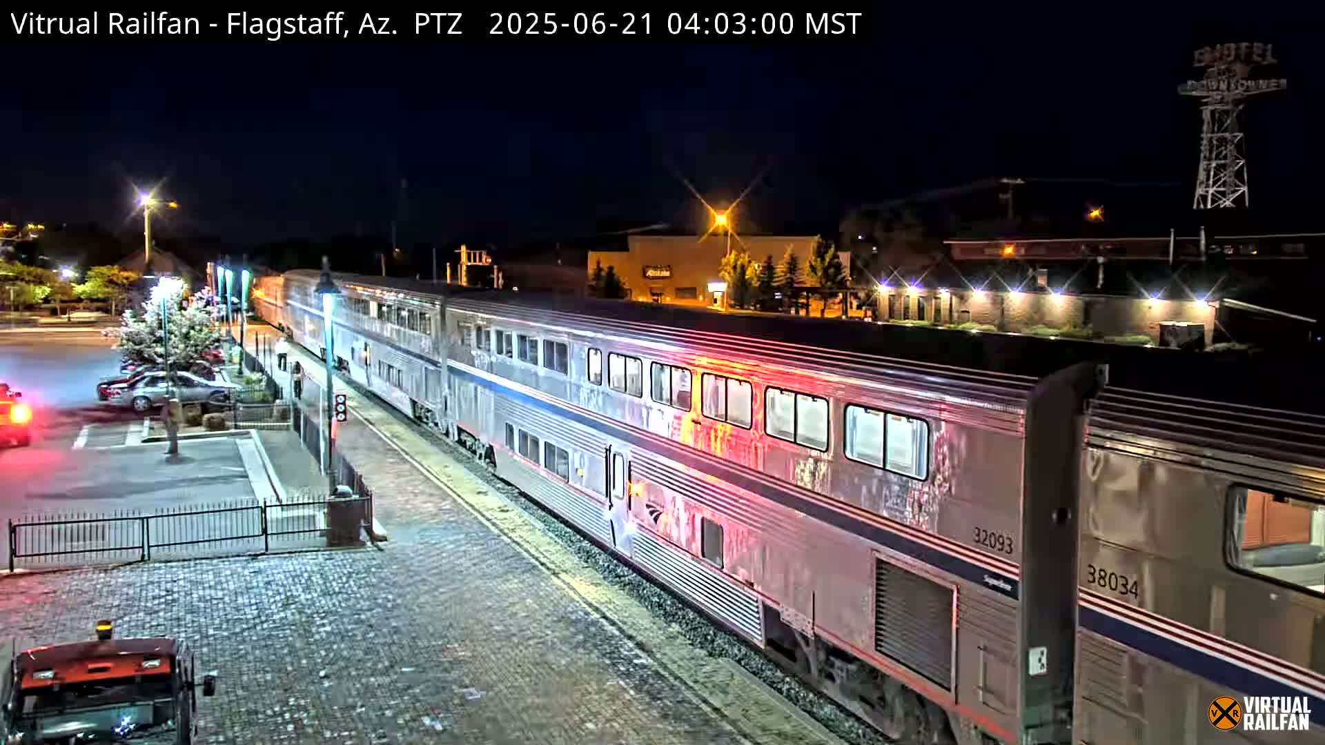 A long passenger train is at a station at night, with cars parked nearby.