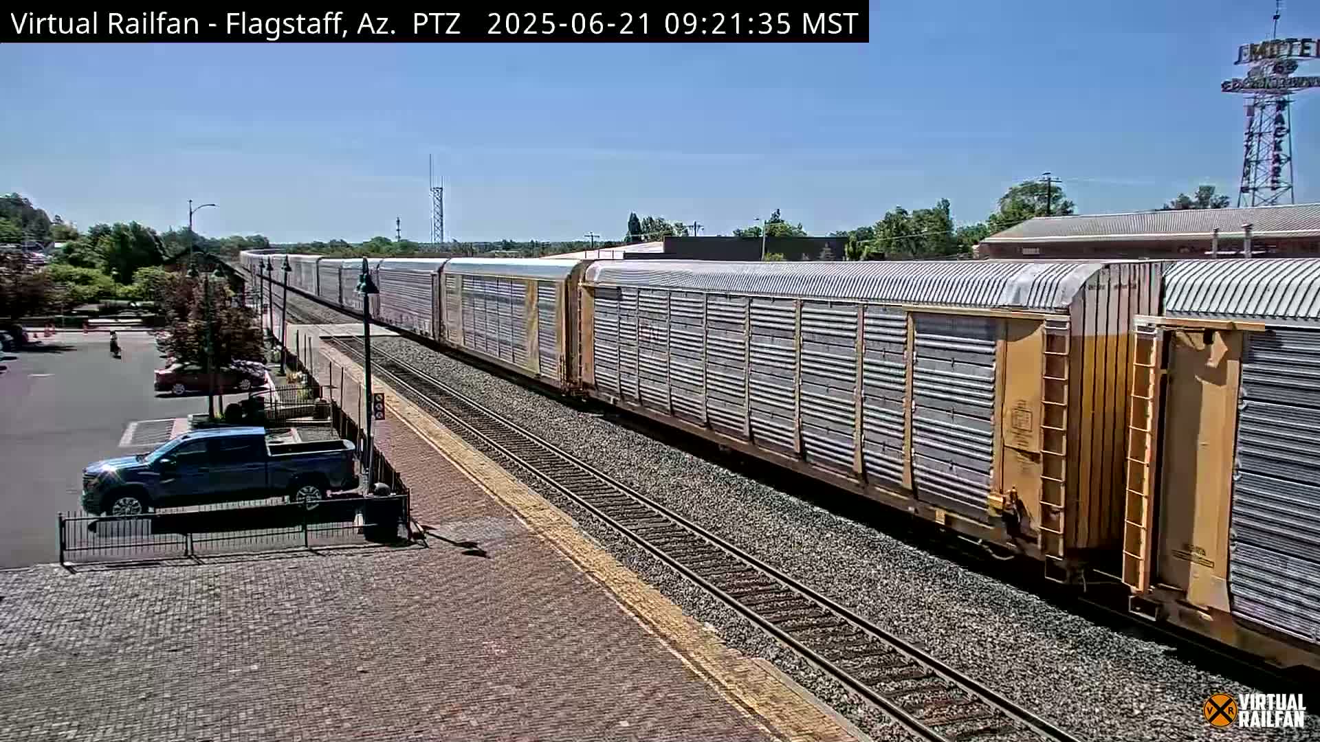 A long freight train passes through a train station on a sunny day.