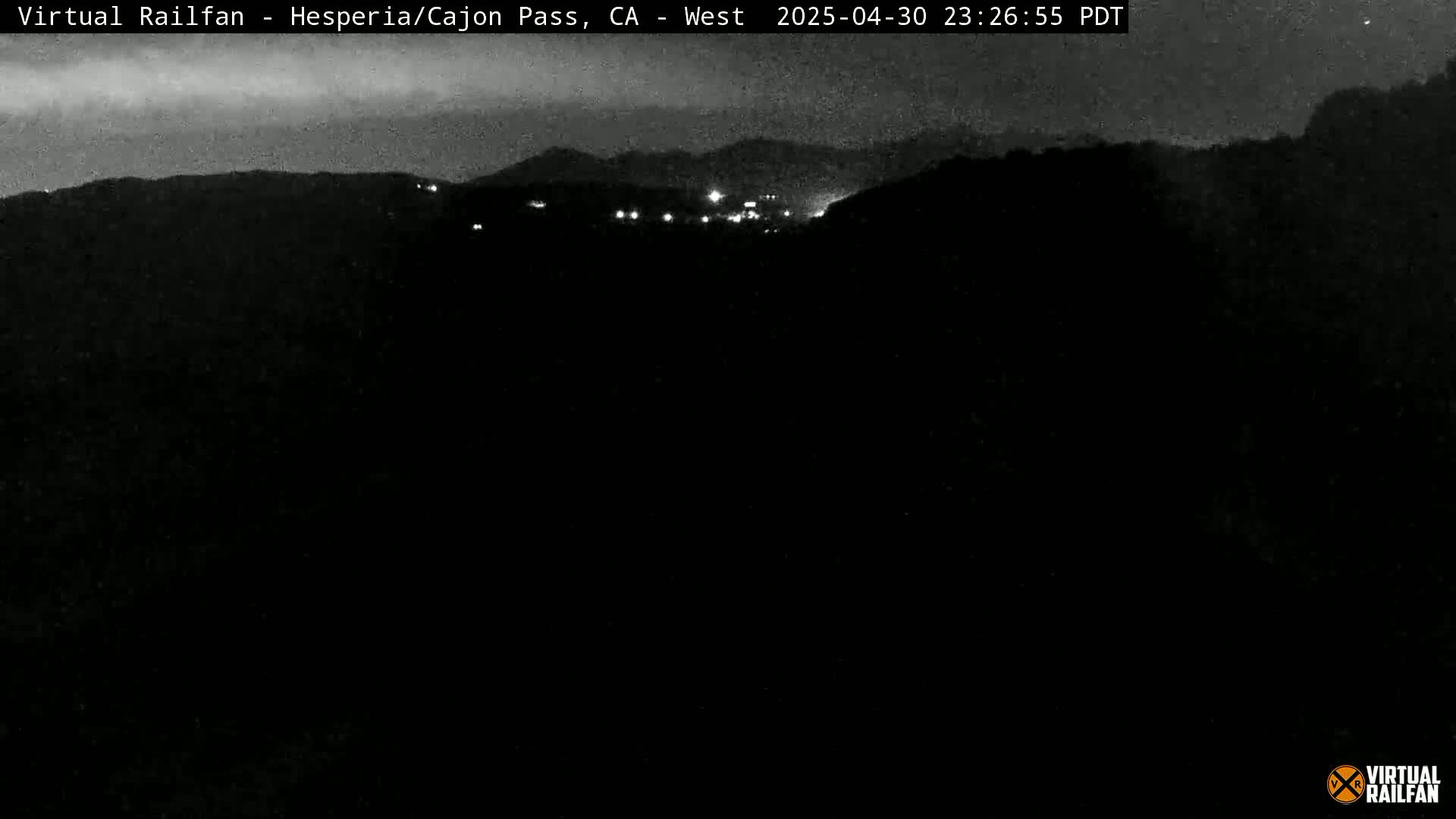 A nighttime view of a dark hillside with a few distant lights under a mostly clear sky.