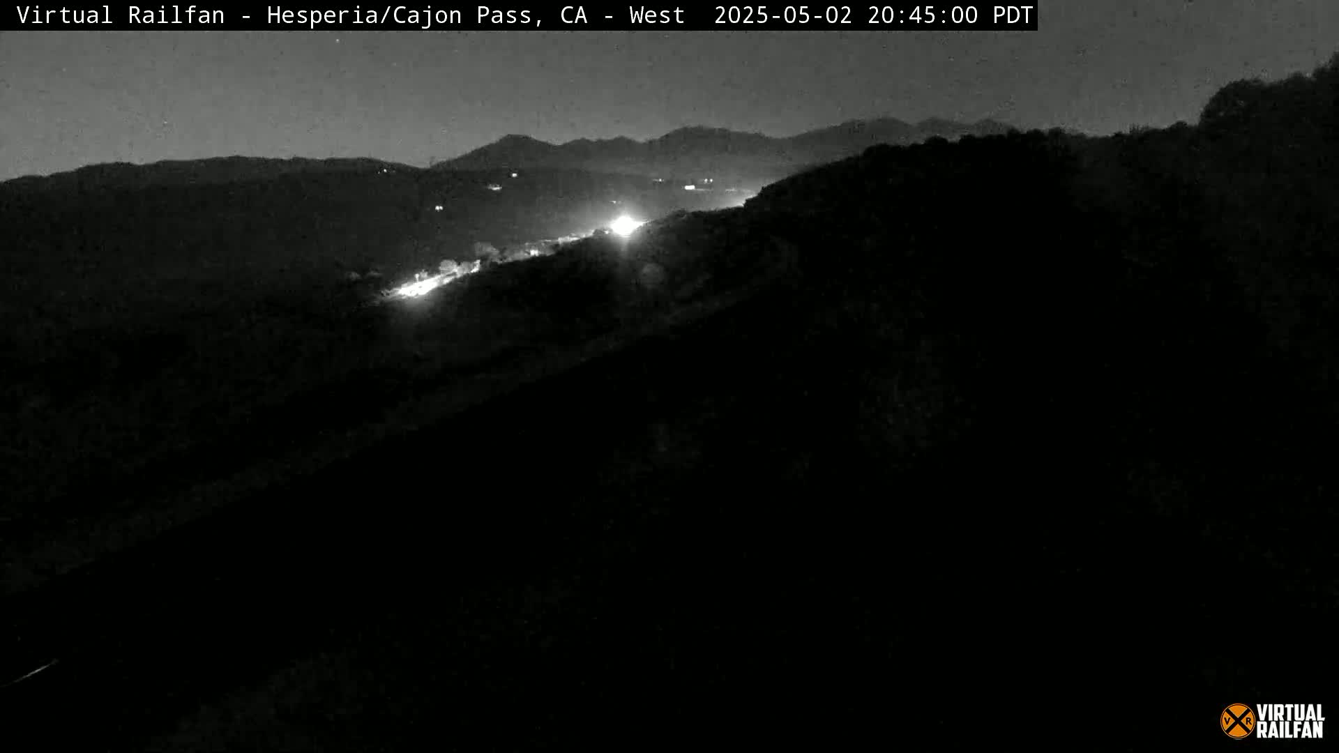 A nighttime, dark view of a highway winding through a hilly landscape.