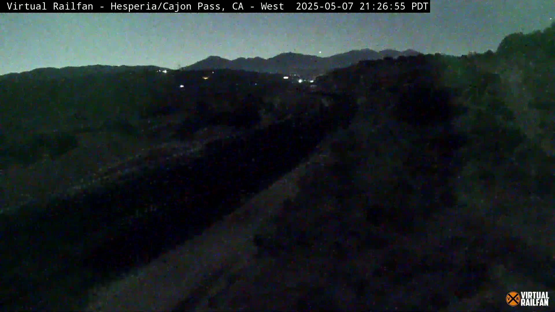 A nighttime, dark view of a hilly landscape under a clear, starry sky.