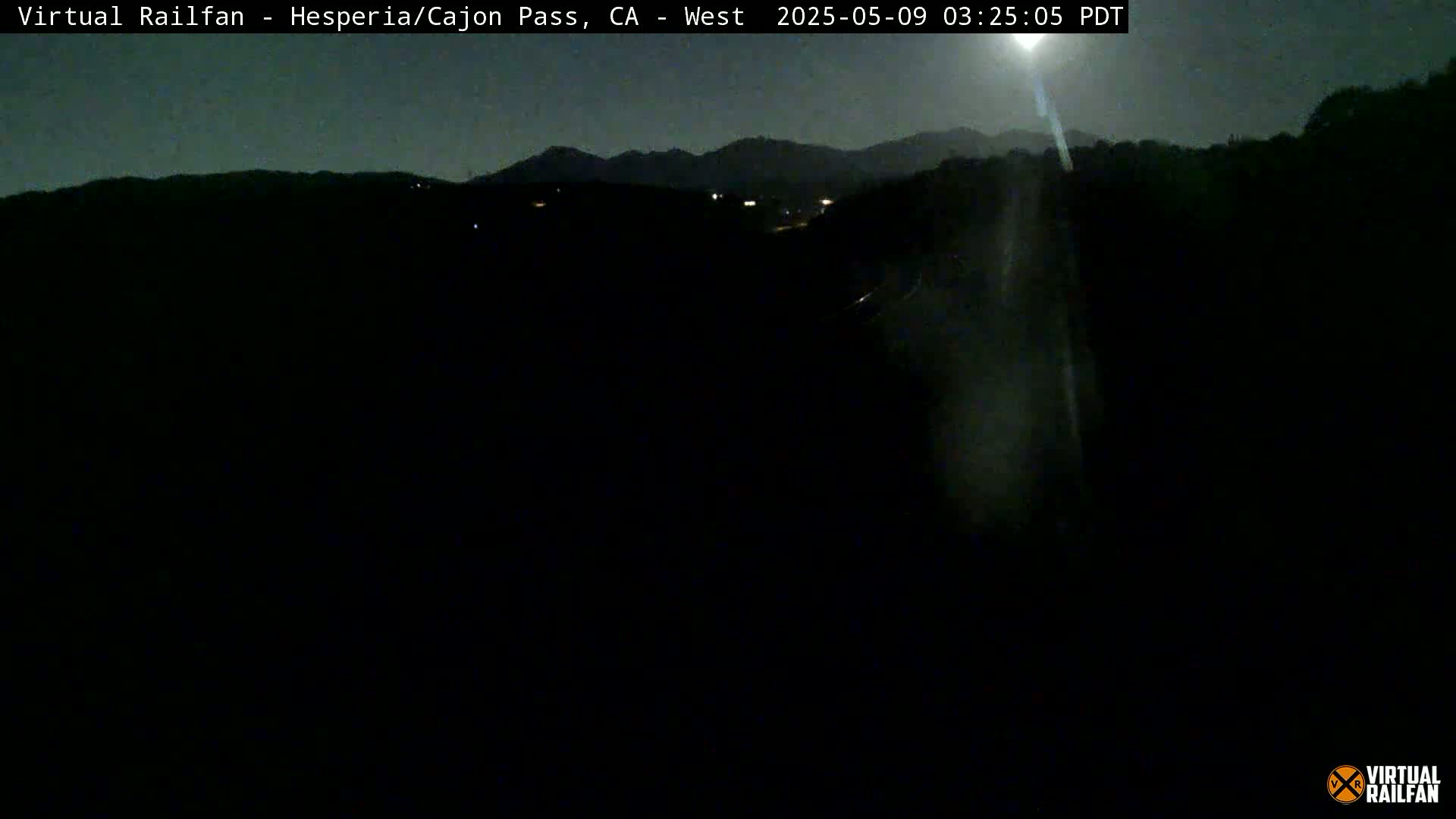 A nighttime, dark view of a landscape with mountains in the distance under a mostly clear sky.