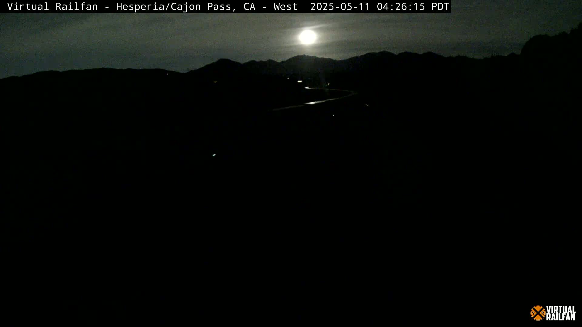 A nighttime view of a dark road winding through a mountainous landscape under a bright moon.