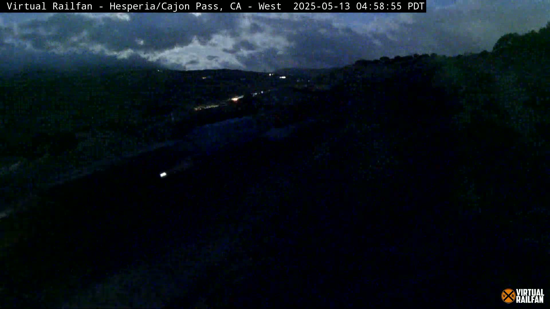 A nighttime, overcast view of a highway and distant hills with sparse vehicle lights visible.