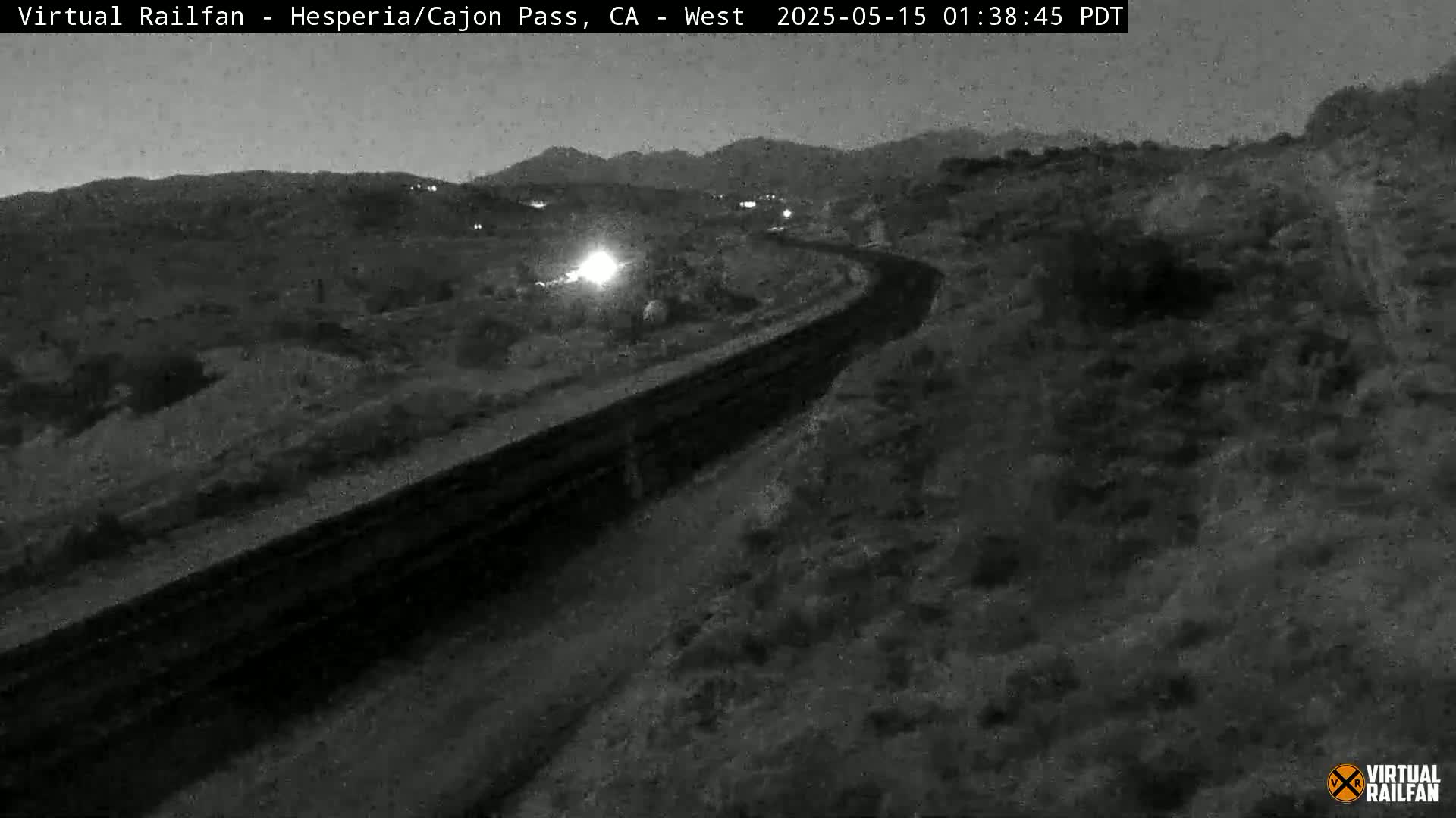 A nighttime, low-light view of a curved road or highway cutting through a desolate, hilly landscape.
