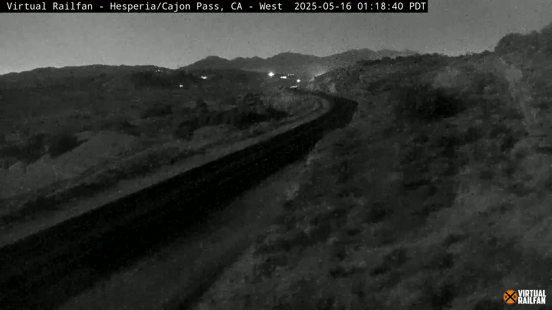 A nighttime, low-light view of a winding road cutting through a dark, hilly landscape.