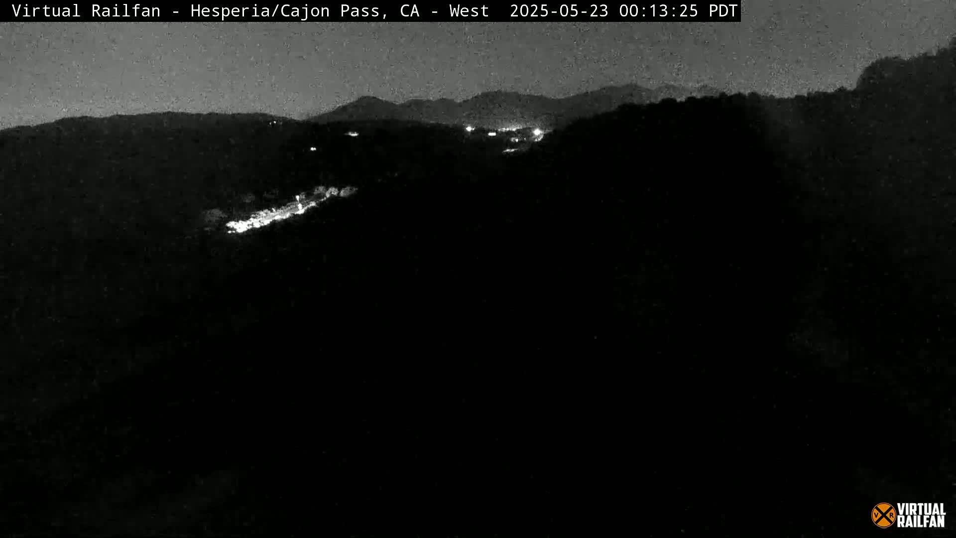 A nighttime view of dimly lit hills and a winding road, with a dark sky.