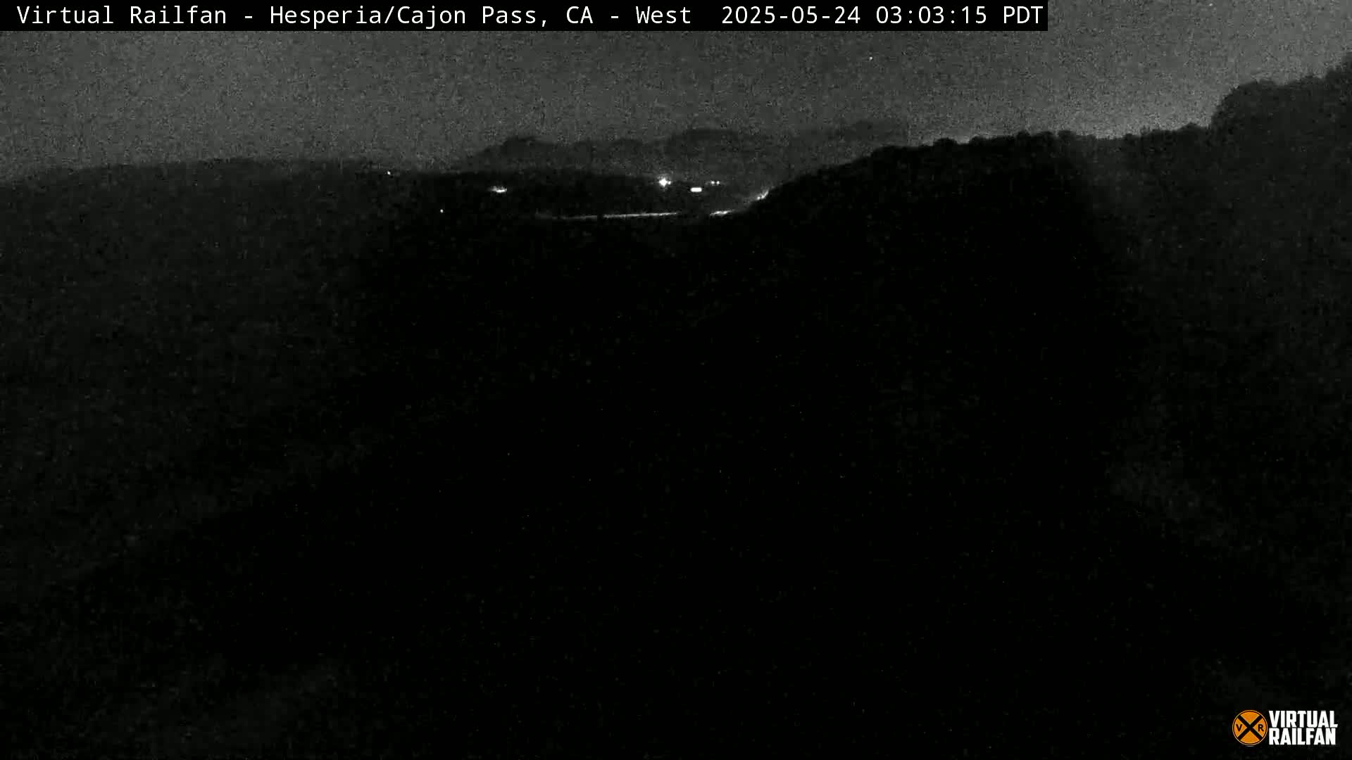 A nighttime, low-light view of a dark landscape with a few distant lights.