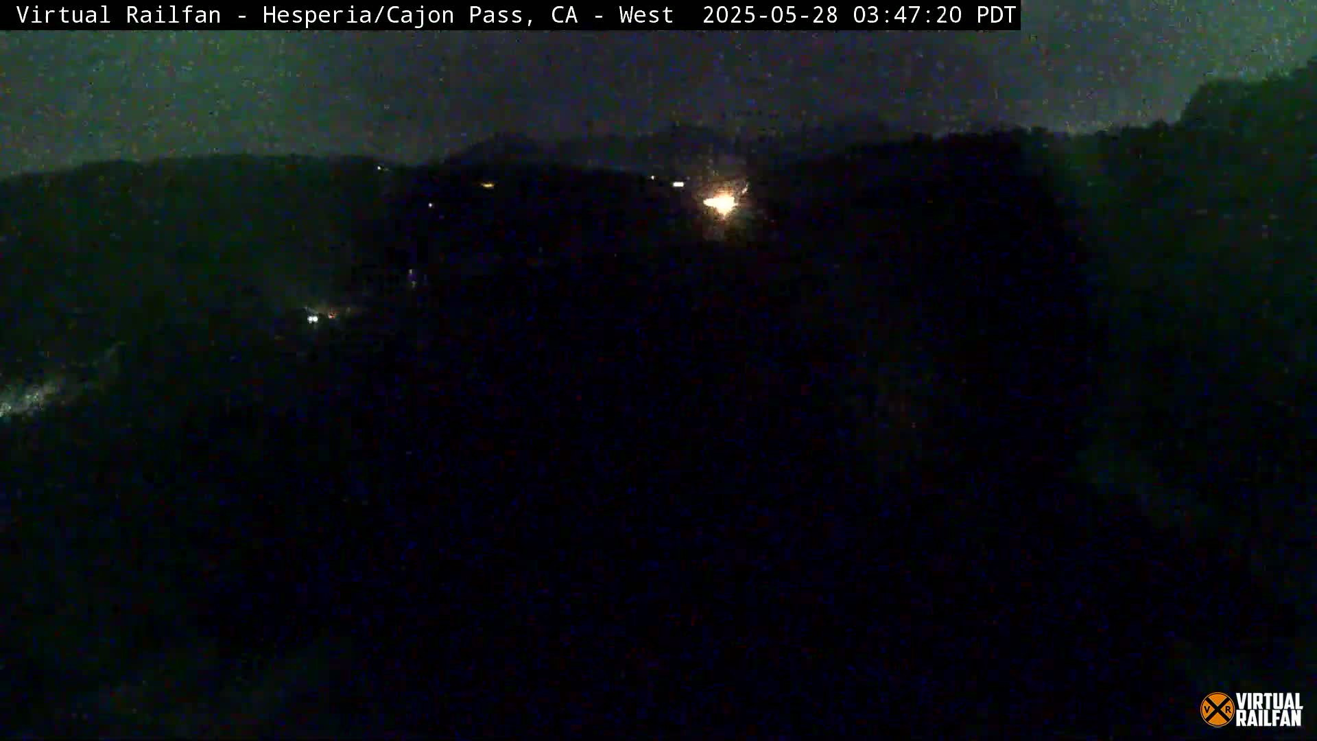 A nighttime, dark view of a landscape with some distant lights, possibly under a slightly cloudy sky.