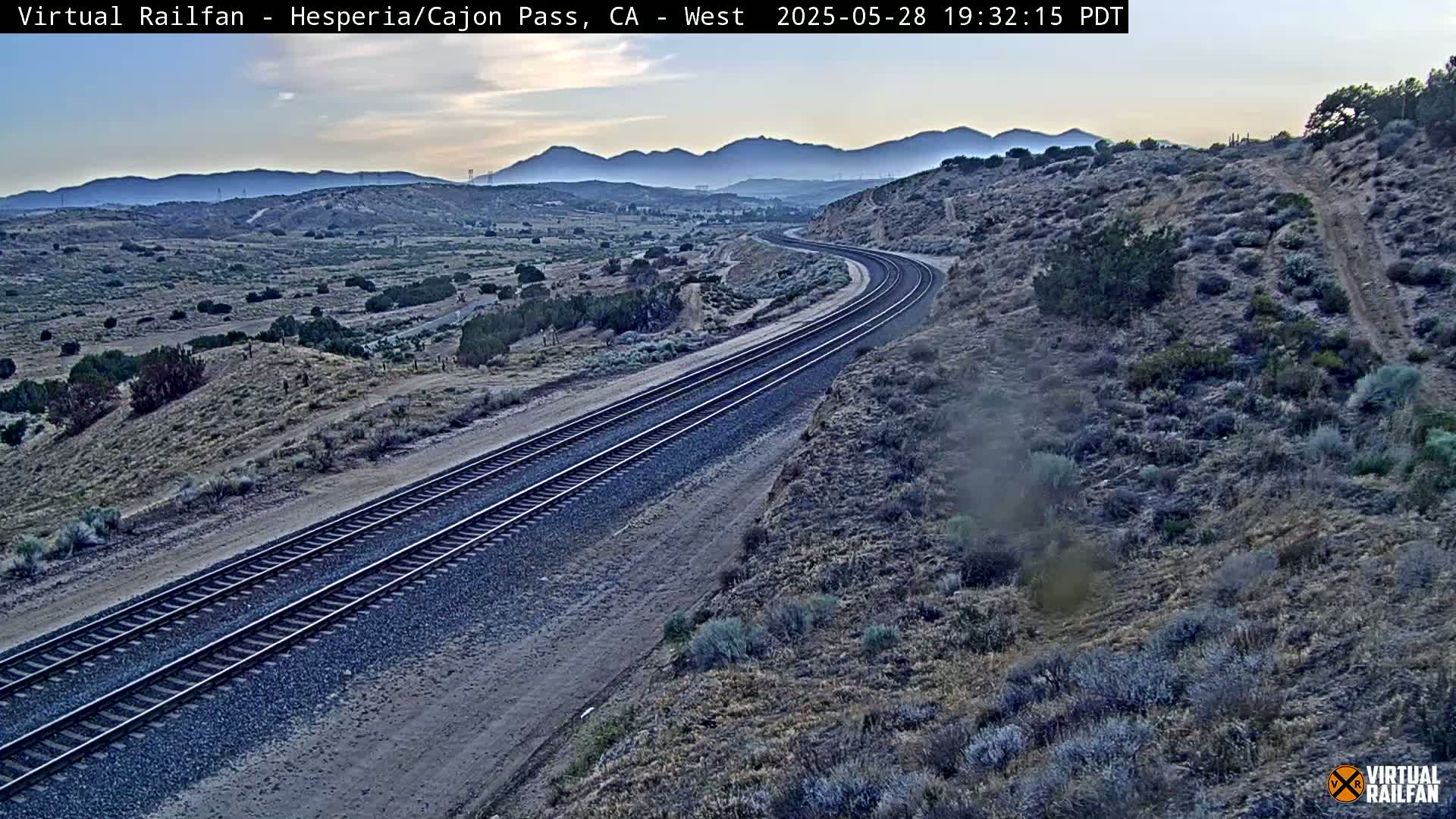 A high-angle, long shot shows a train track curving through a desert landscape under a twilight sky.