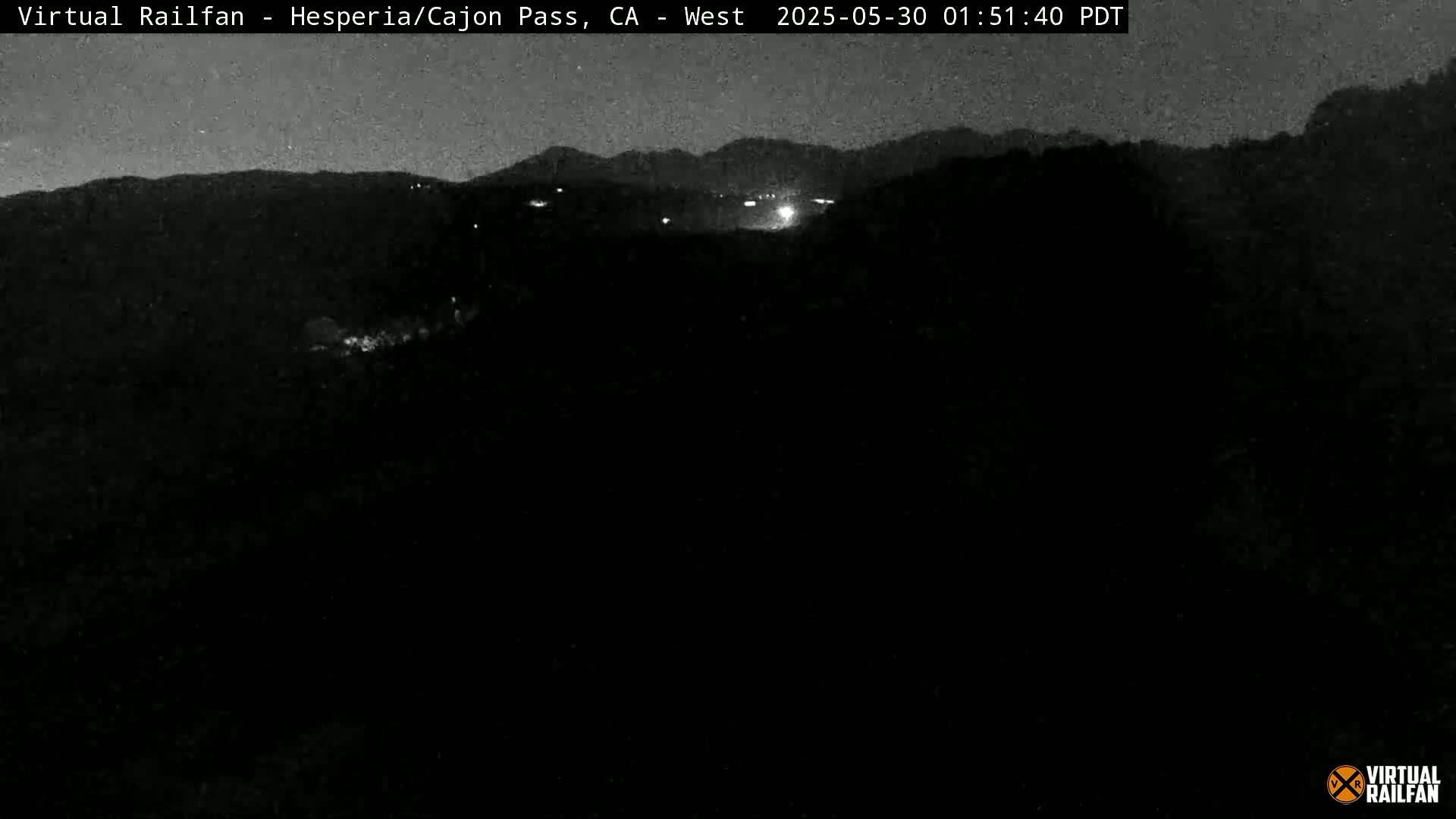 A nighttime, low-light view of dark hills and distant faint lights under a clear, dark sky.