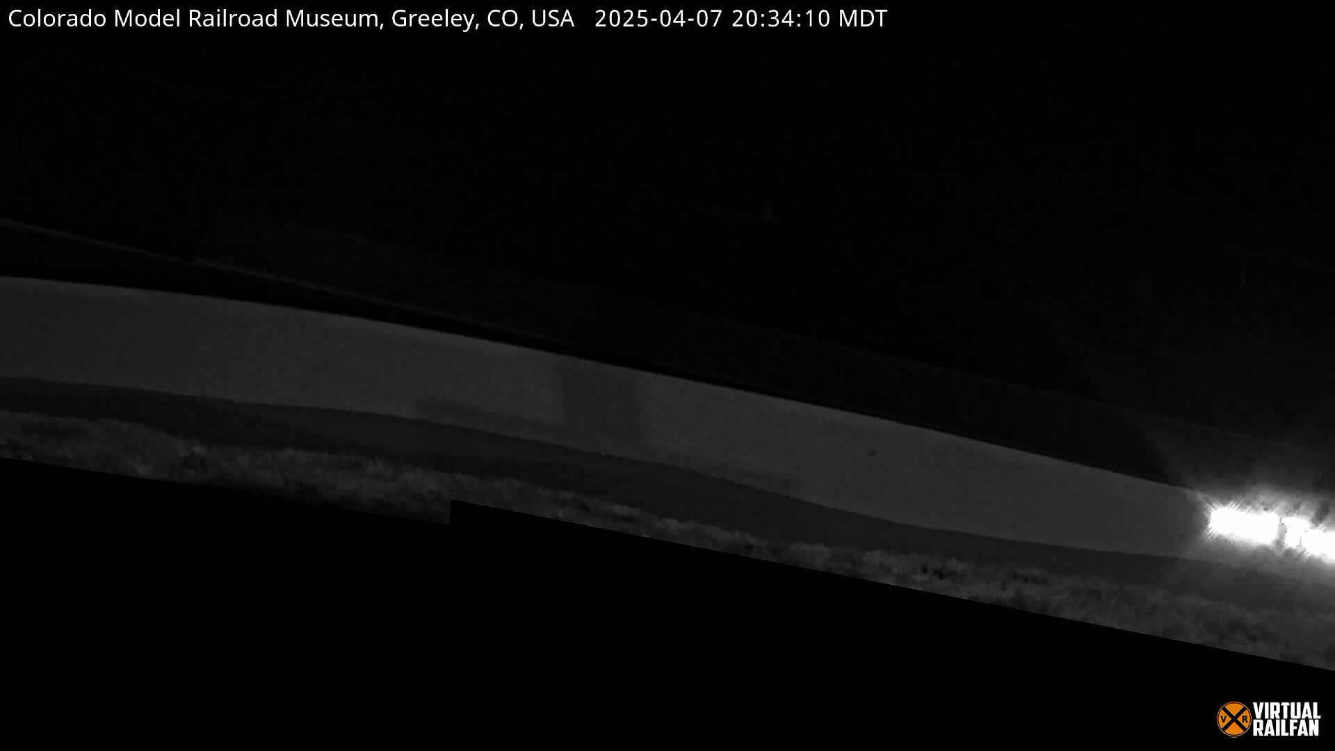 A low-light nighttime image shows a long, horizontal structure, possibly a roadway or track, with a bright light source visible in the far right.