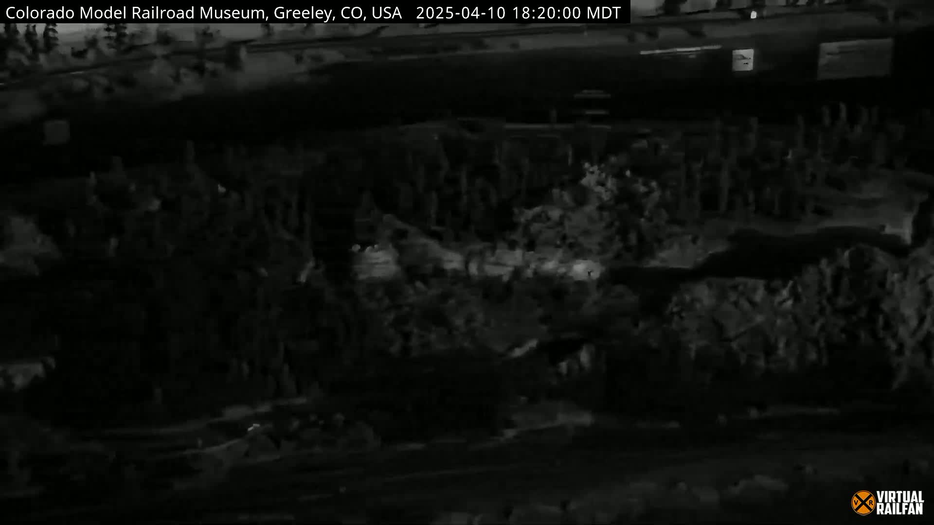 A nighttime, low-light, grainy image shows a dark, possibly outdoor, area with indistinct shapes and textures suggesting vegetation or debris.