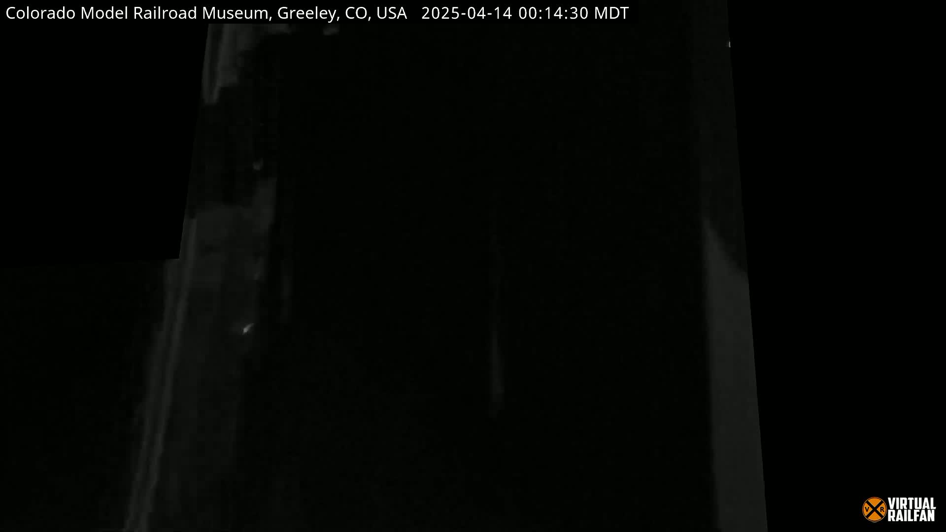 A very dark, nighttime image shows a dimly lit, tall, thin, vertical object.