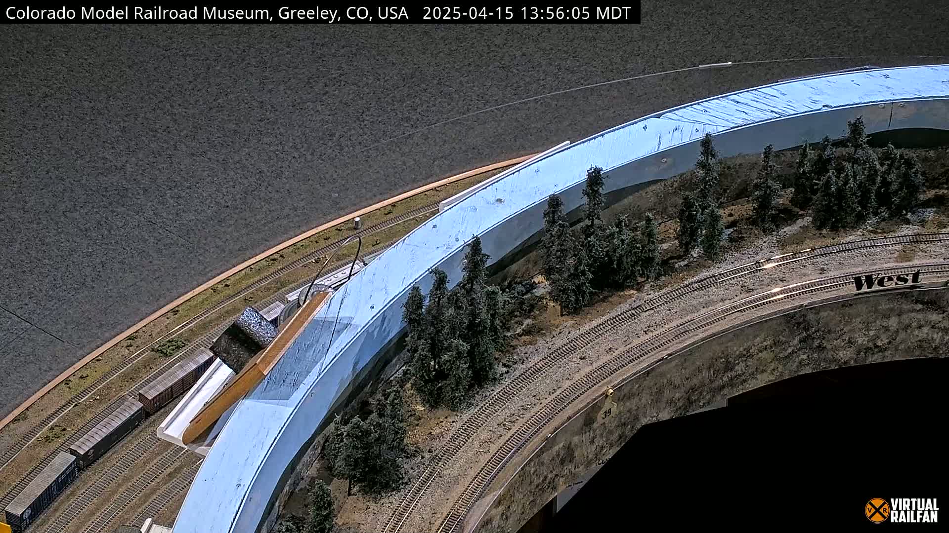 An overhead view of a model train set with a curved track, miniature trees, and a light blue wall.