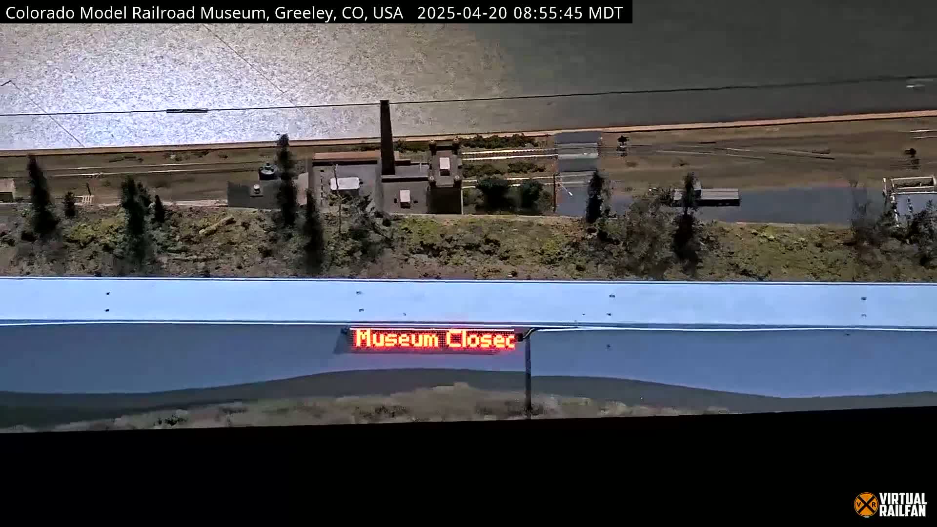 A model railroad scene with a body of water in the background and a sign indicating the museum is closed.