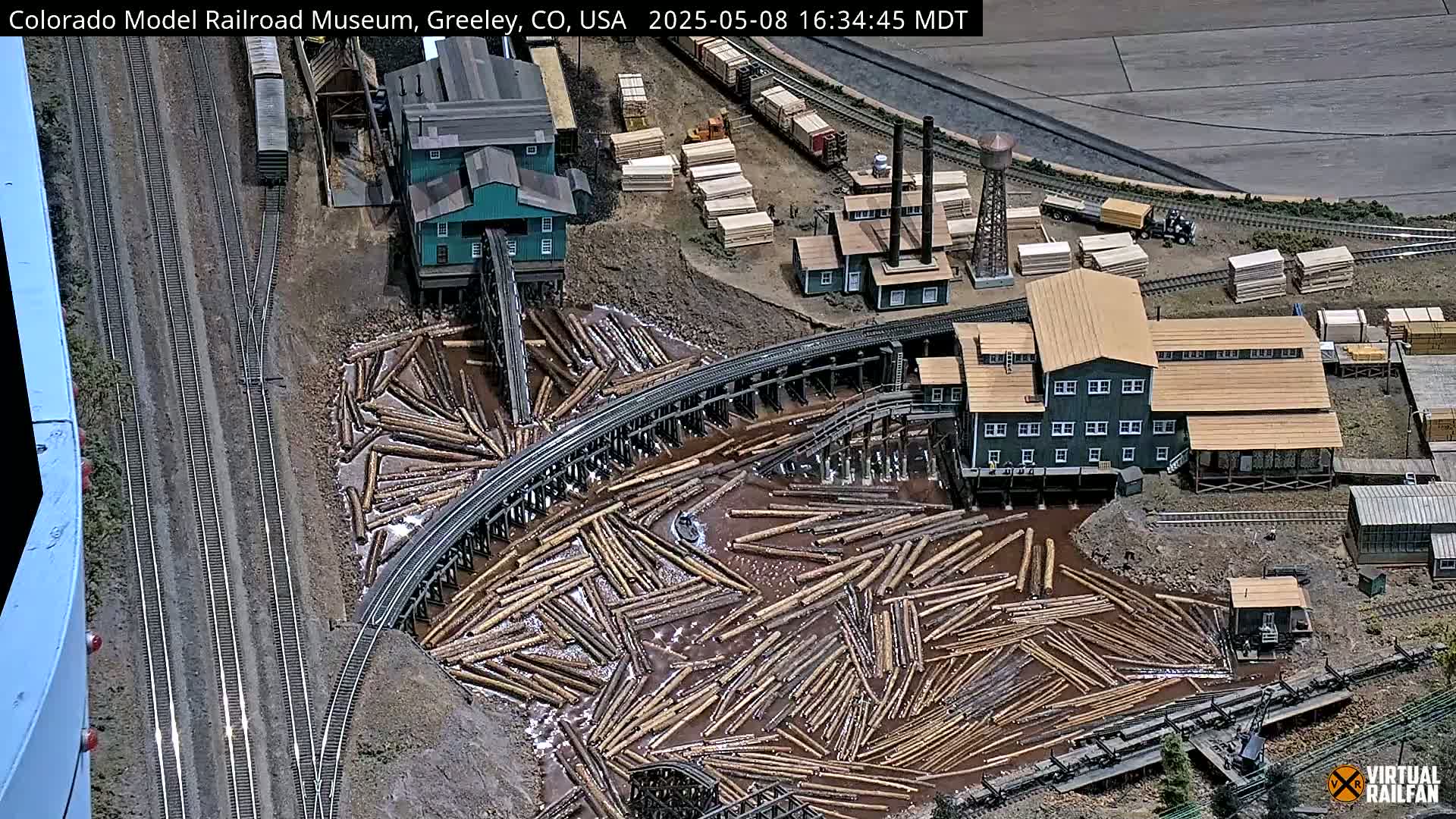 A detailed model of a lumber mill and railroad, showing logs floating in water next to a train track and buildings.